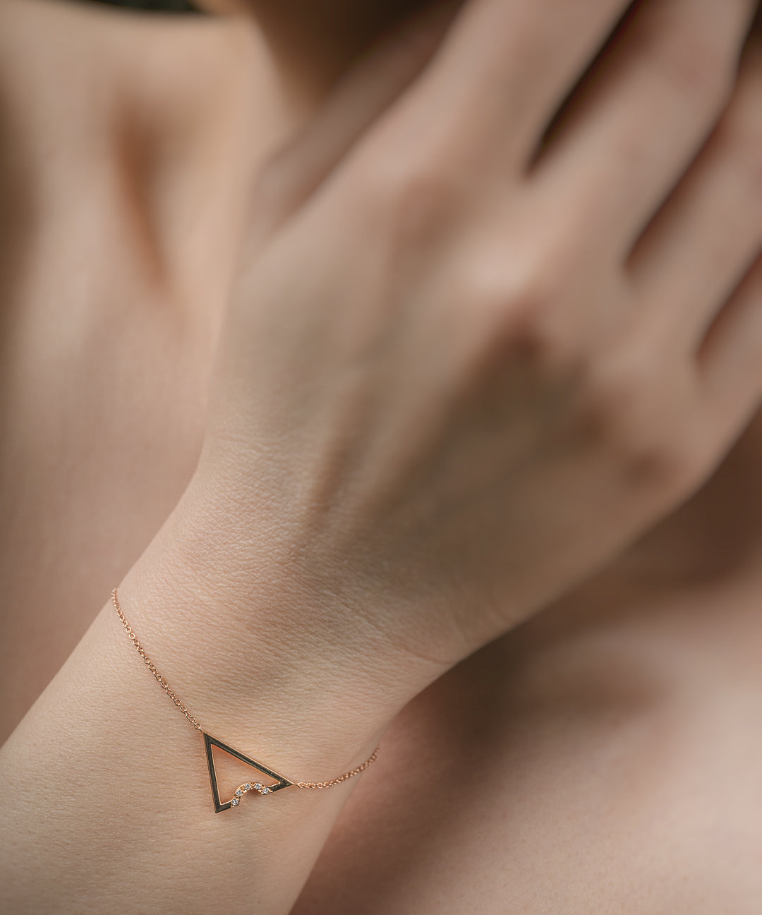 Rose gold triangle anklet on a wrist with a blurred background