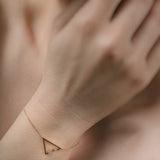 Rose gold triangle anklet on a wrist with a blurred background