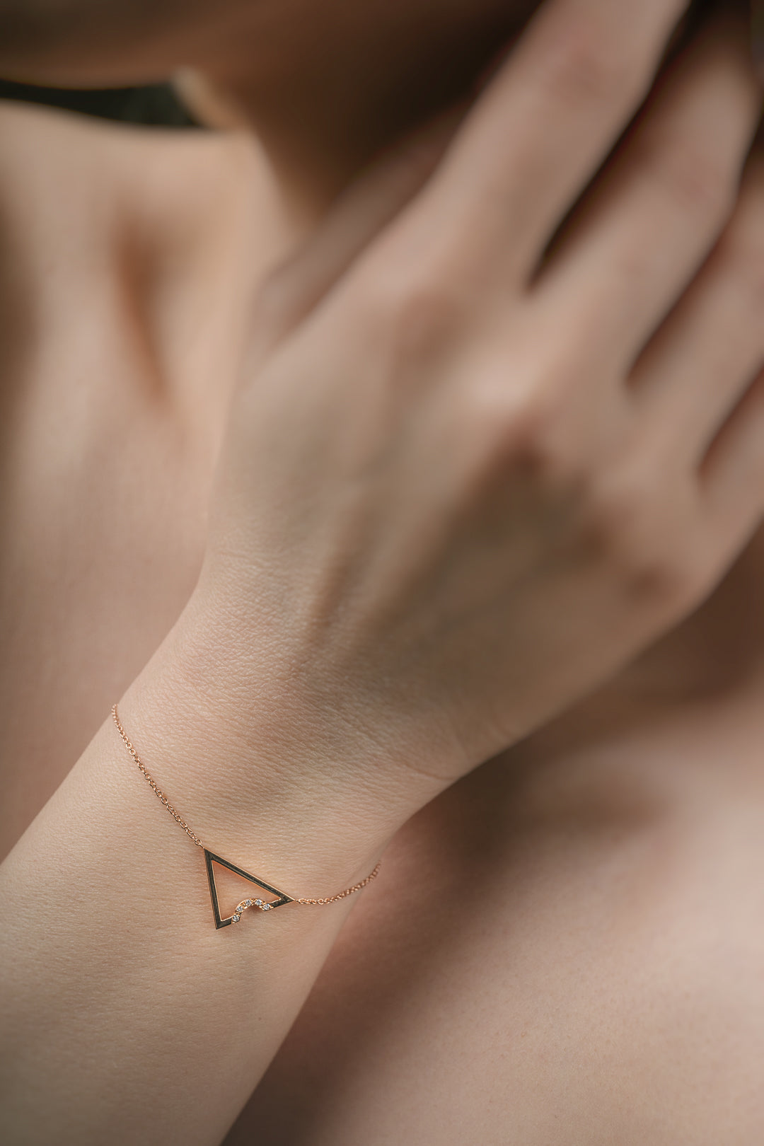 Rose gold triangle anklet on a wrist with a blurred background