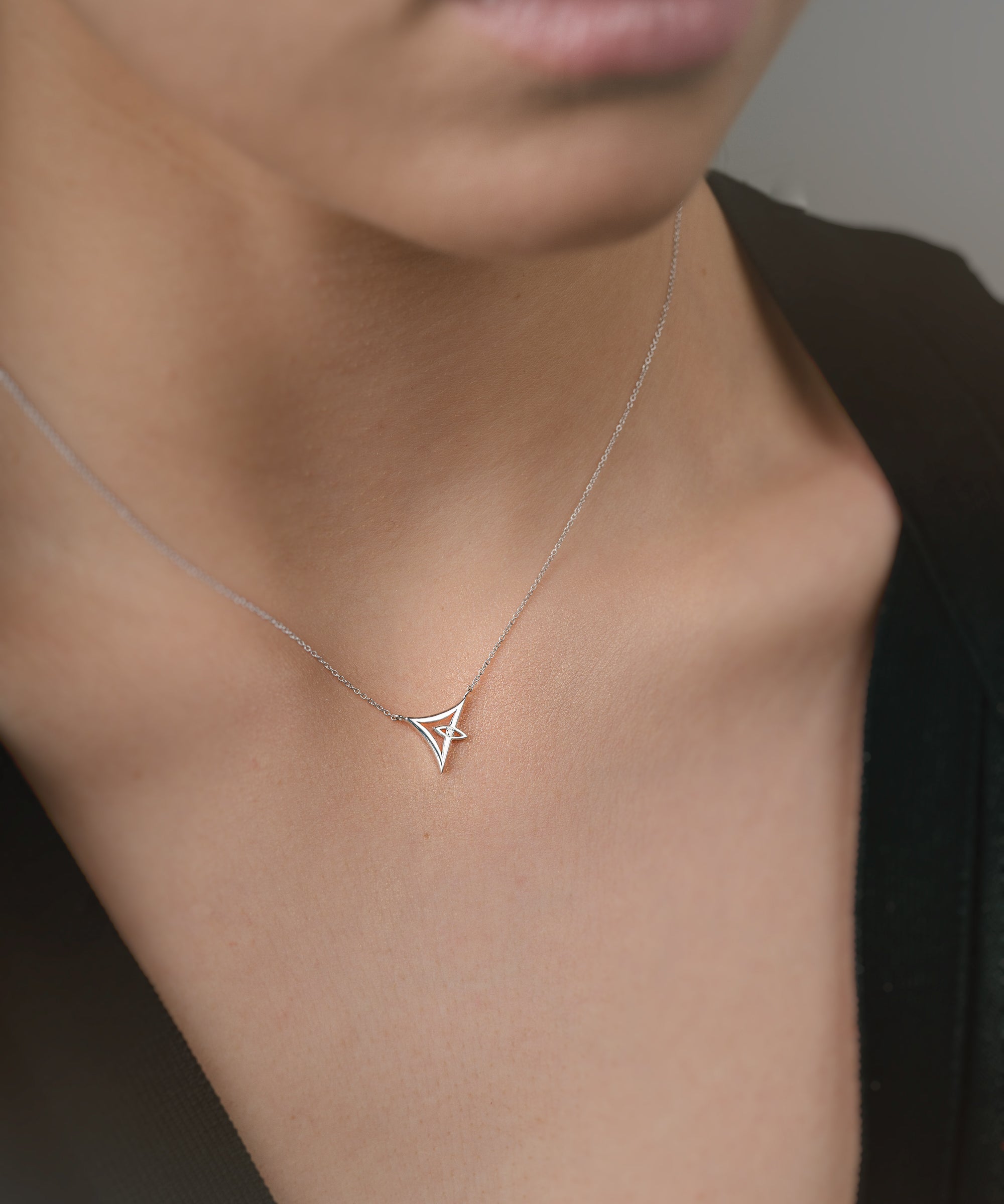 Person wearing a delicate white gold necklace with a triangle pendant.