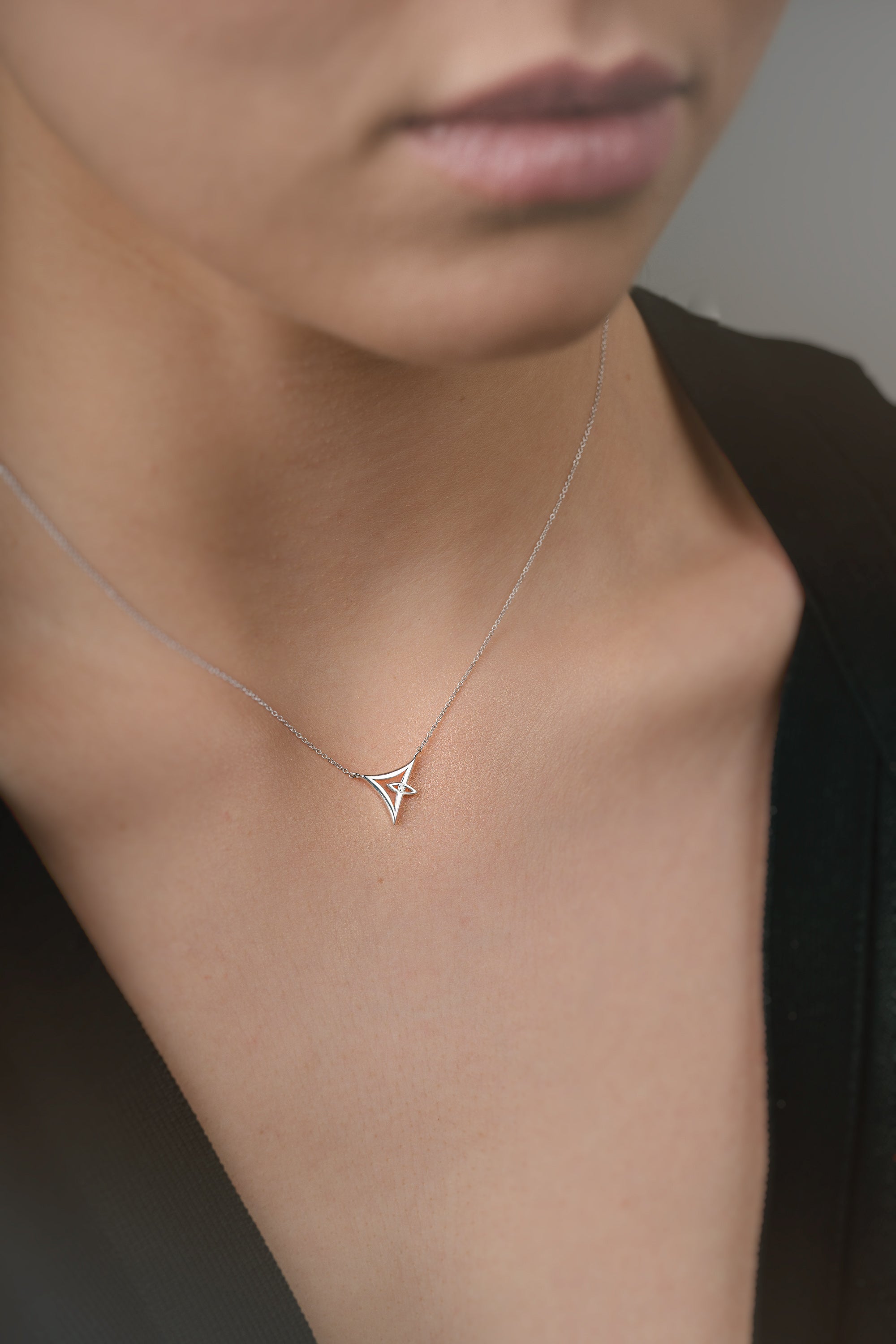 Person wearing a delicate white gold necklace with a triangle pendant.