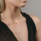 Woman wearing a gold necklace with a triangle pendant against a neutral background