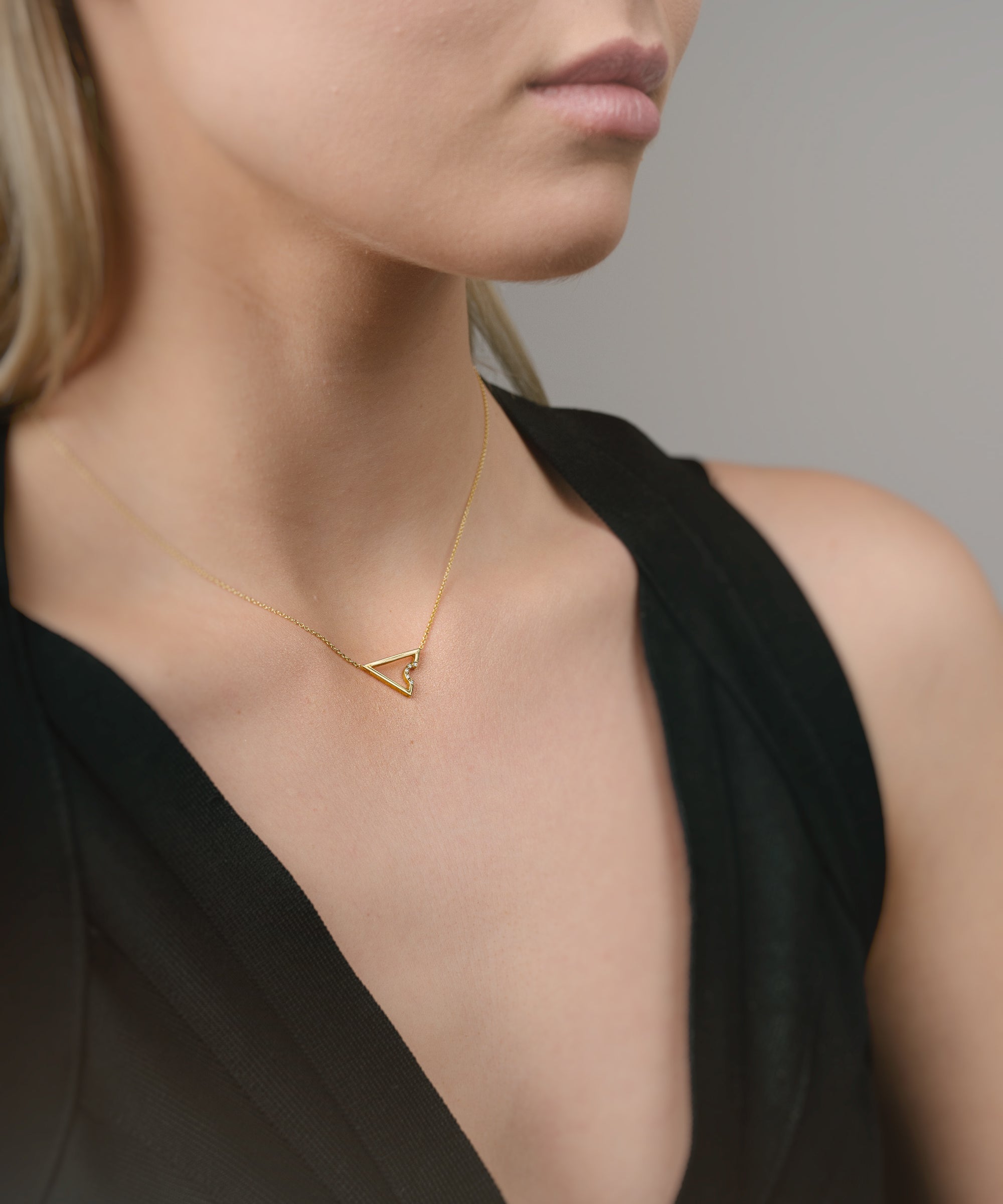 Woman wearing a gold necklace with a triangle pendant against a neutral background