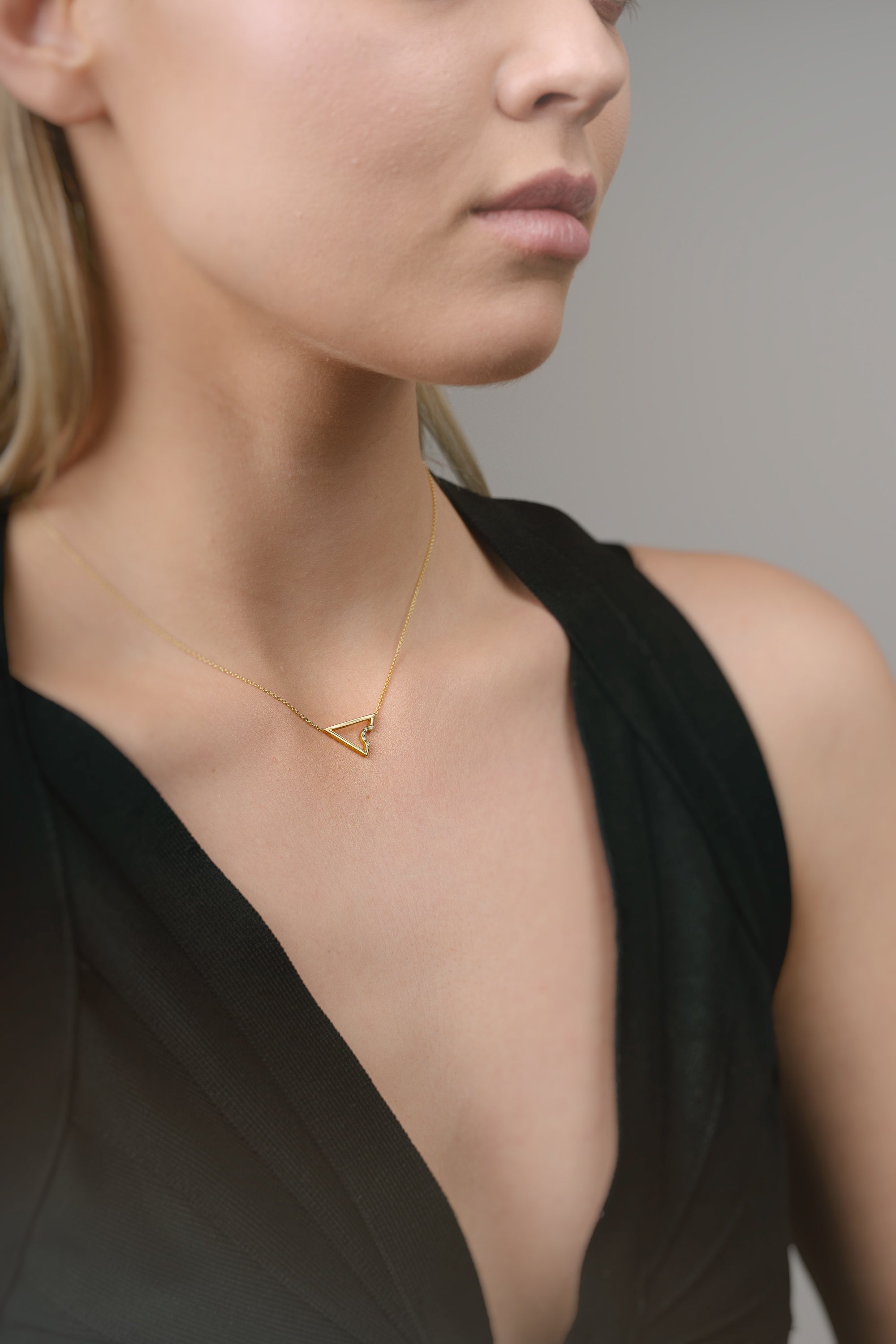 Woman wearing a gold necklace with a triangle pendant against a neutral background