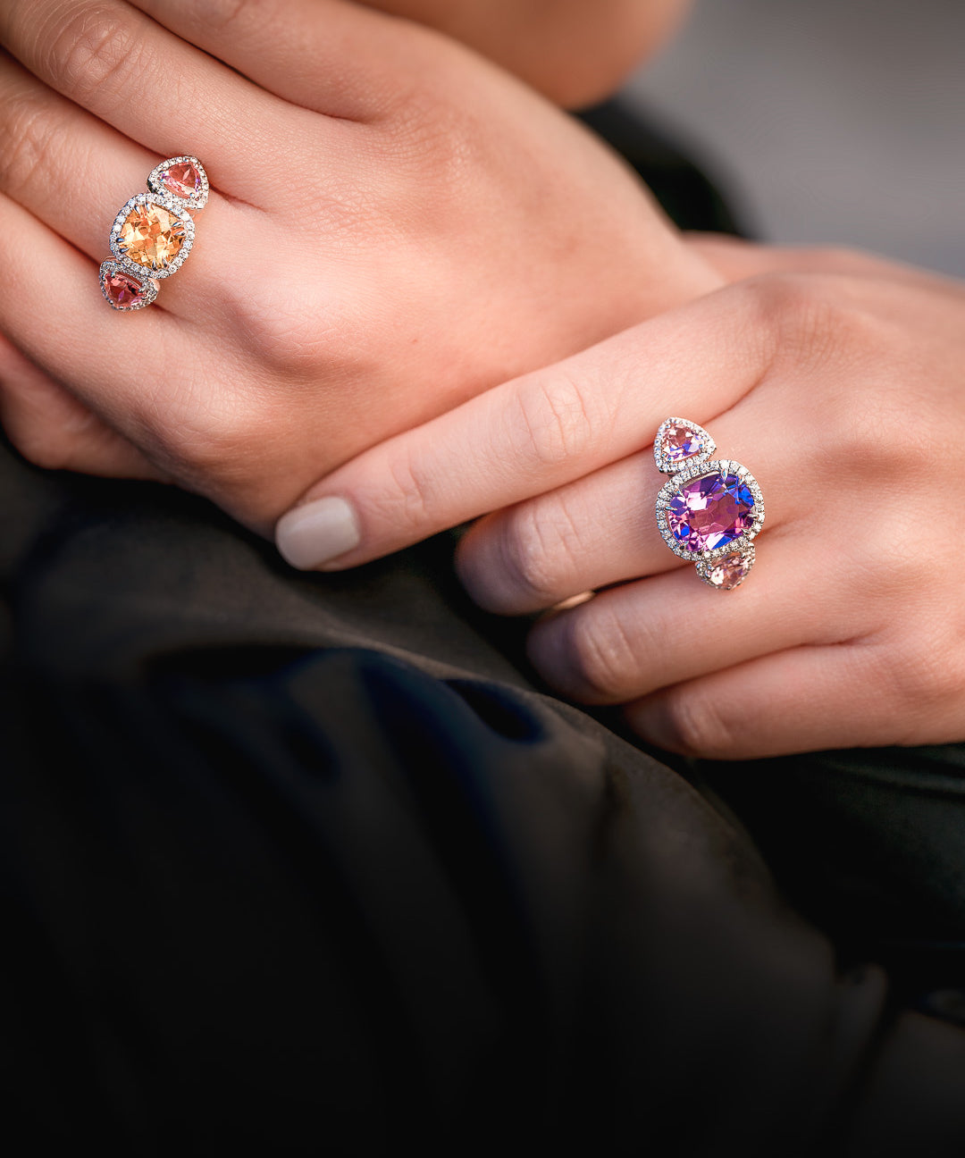 Close-up of hands wearing two colorful gemstone rings against a dark background