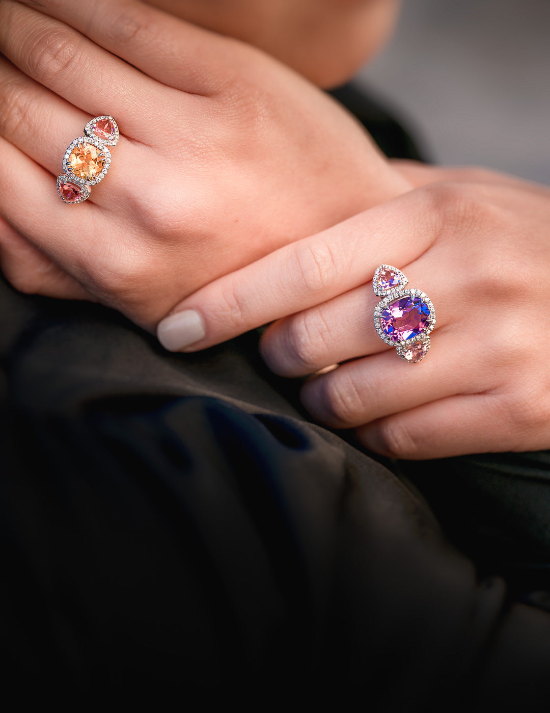 Close-up of hands wearing two colorful gemstone rings against a dark background
