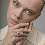 Woman wearing a ring with a purple gemstone against a neutral background