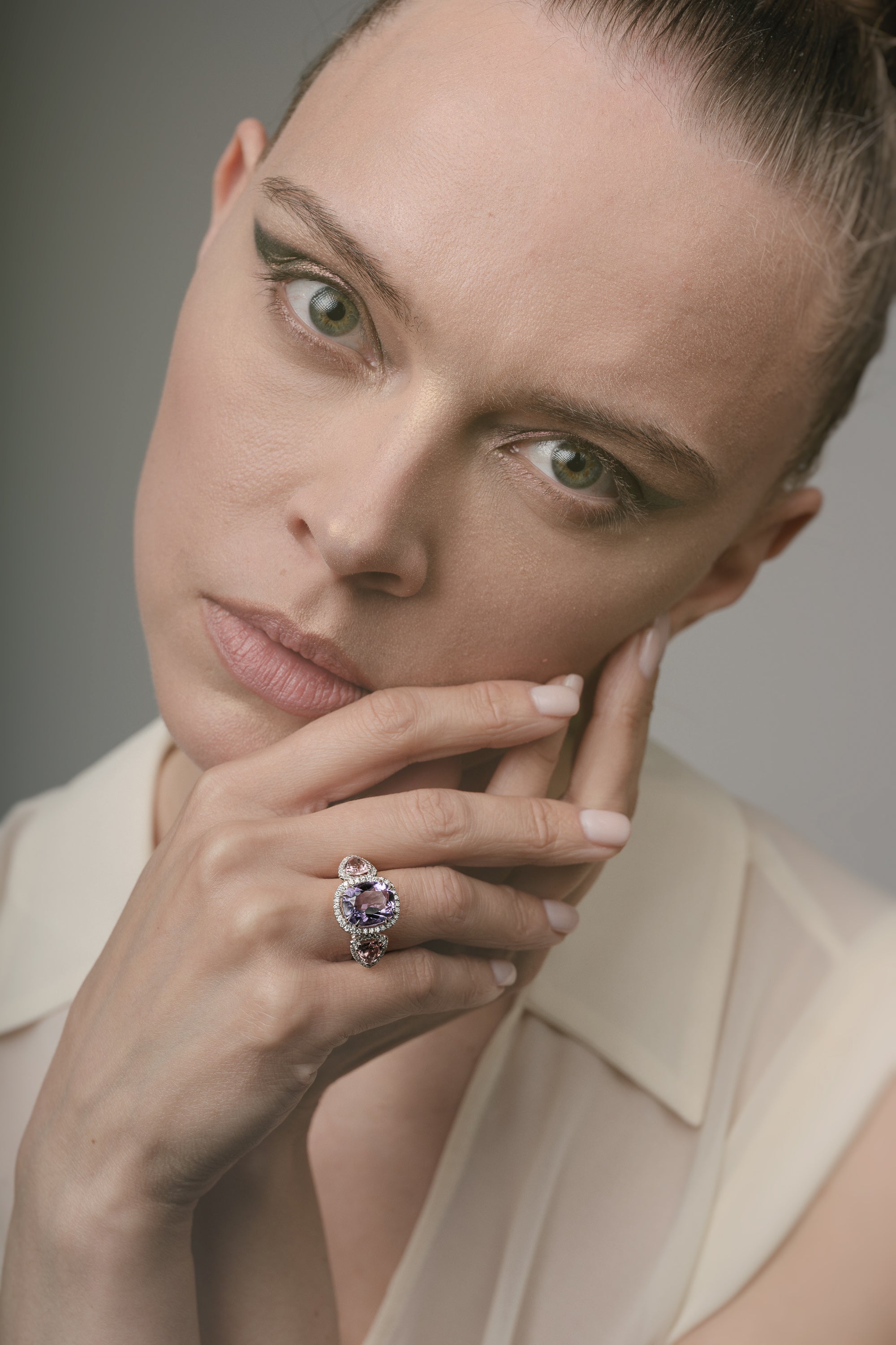 Woman wearing a ring with a purple gemstone against a neutral background