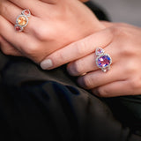 Close-up of hands wearing two colorful gemstone rings against a dark background
