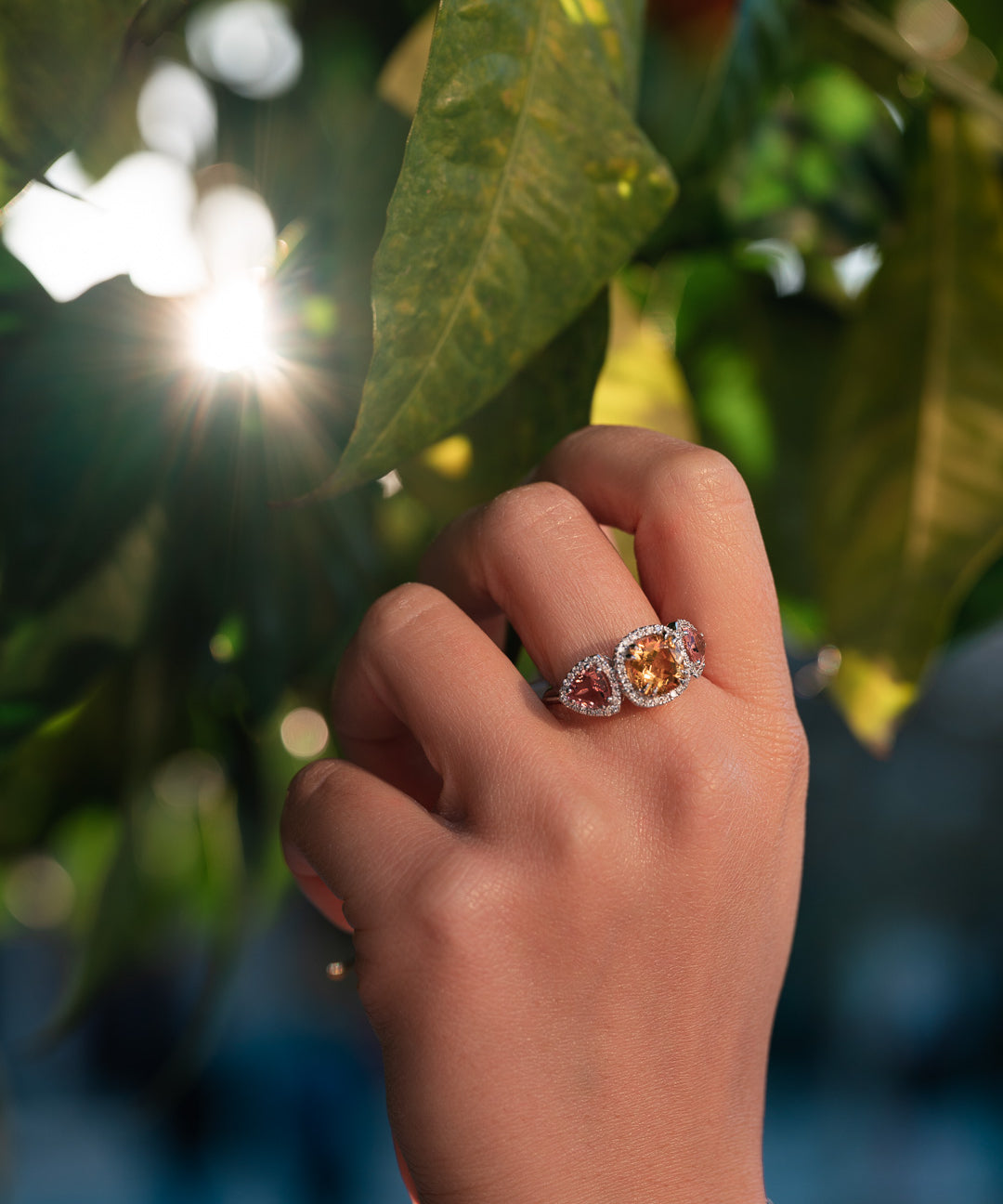 Hand wearing a ring with yellow citrine and pink tourmalines against a blurred natural background