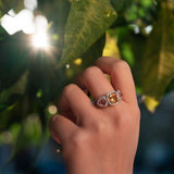 Hand wearing a ring with yellow citrine and pink tourmalines against a blurred natural background