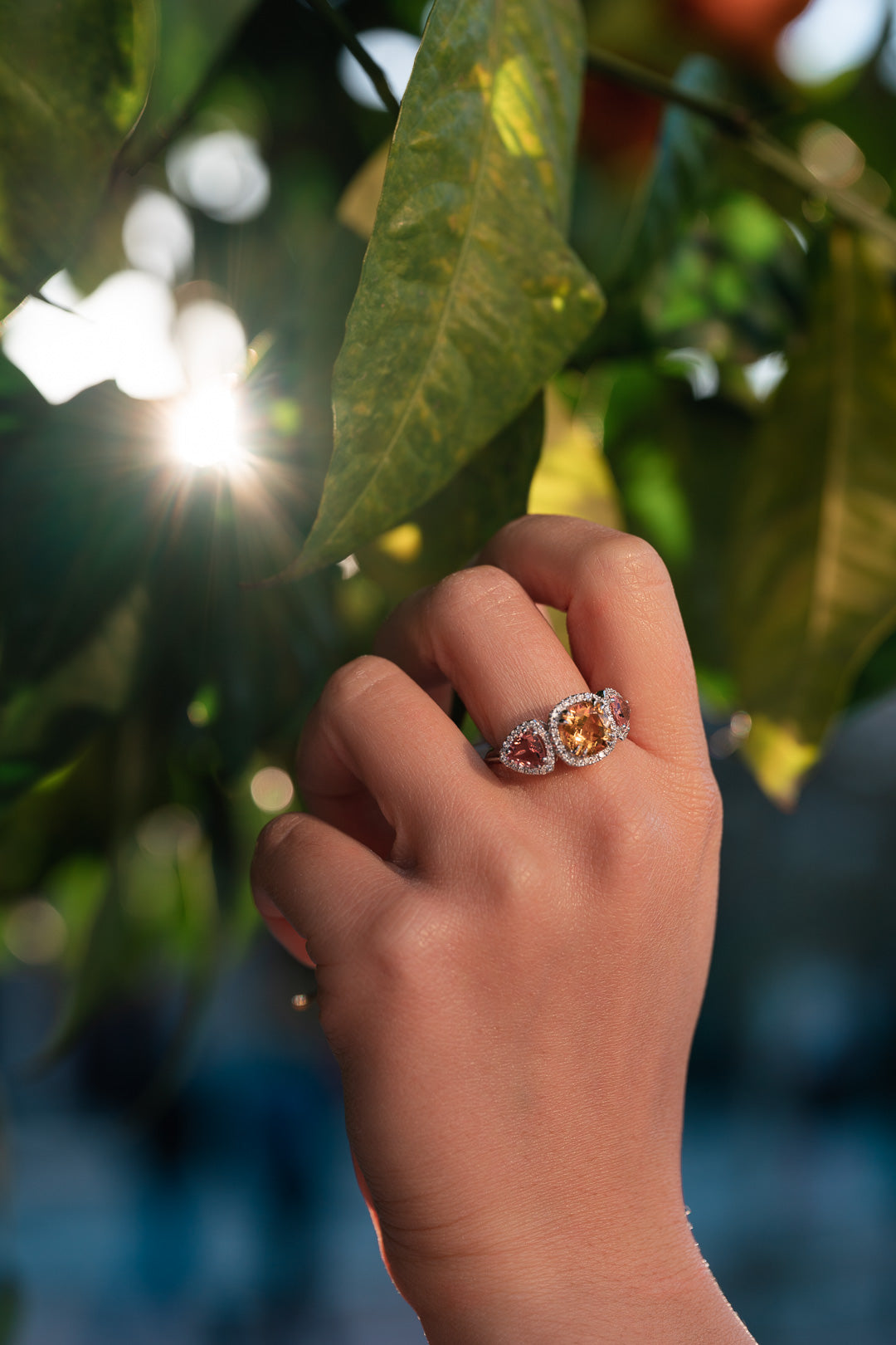 Hand wearing a ring with yellow citrine and pink tourmalines against a blurred natural background