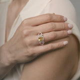 Close-up of a hand wearing a ring with a citrine and tourmaline gemstones on a neutral background
