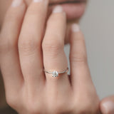 Close-up of a hand wearing a white-gold engagement ring with a diamond on a neutral background