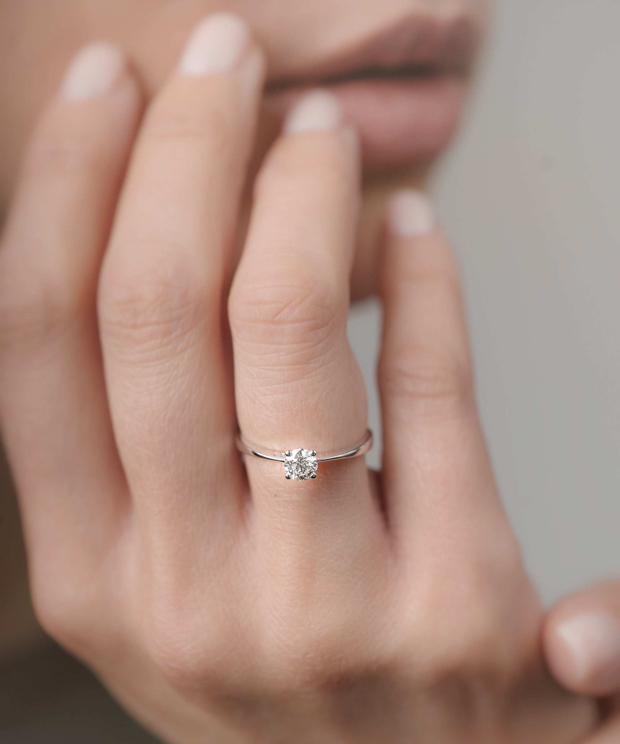 Close-up of a hand wearing a white-gold engagement ring with a diamond on a neutral background