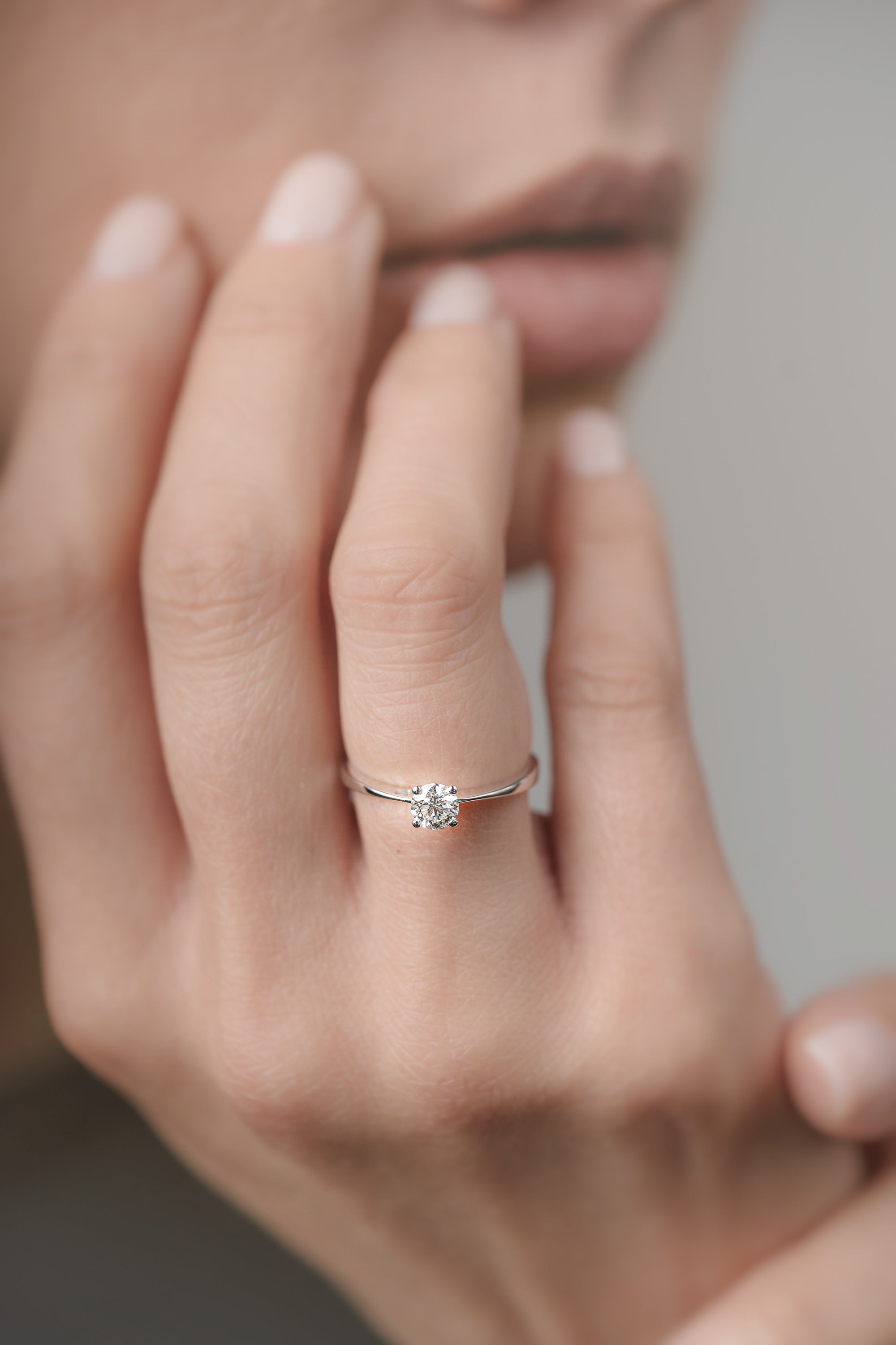 Close-up of a hand wearing a white-gold engagement ring with a diamond on a neutral background