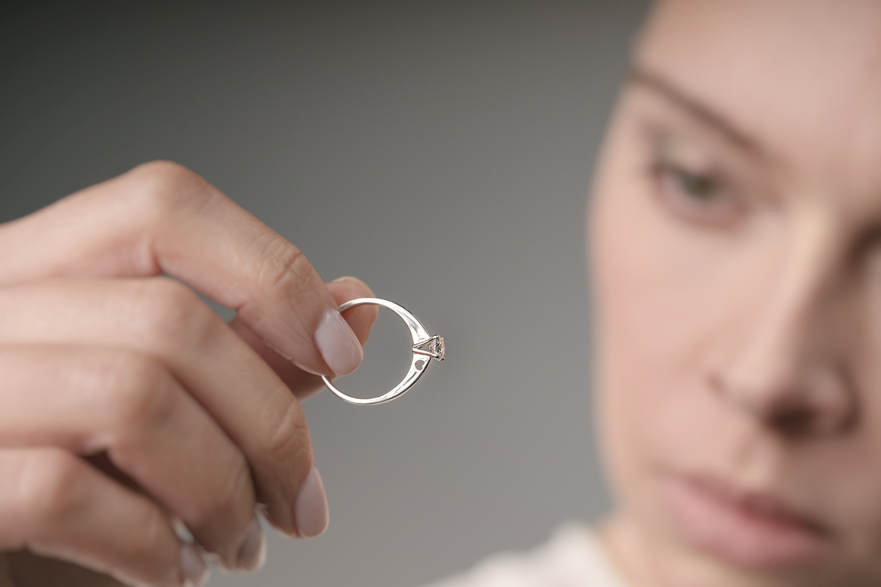 Person holding an engagement ring against a neutral background