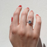 Hand wearing a diamond halo ring with a center aquamarine gemstone on a plain background
