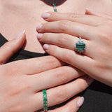 Close-up of a person wearing three emerald green gemstone rings on a plain background