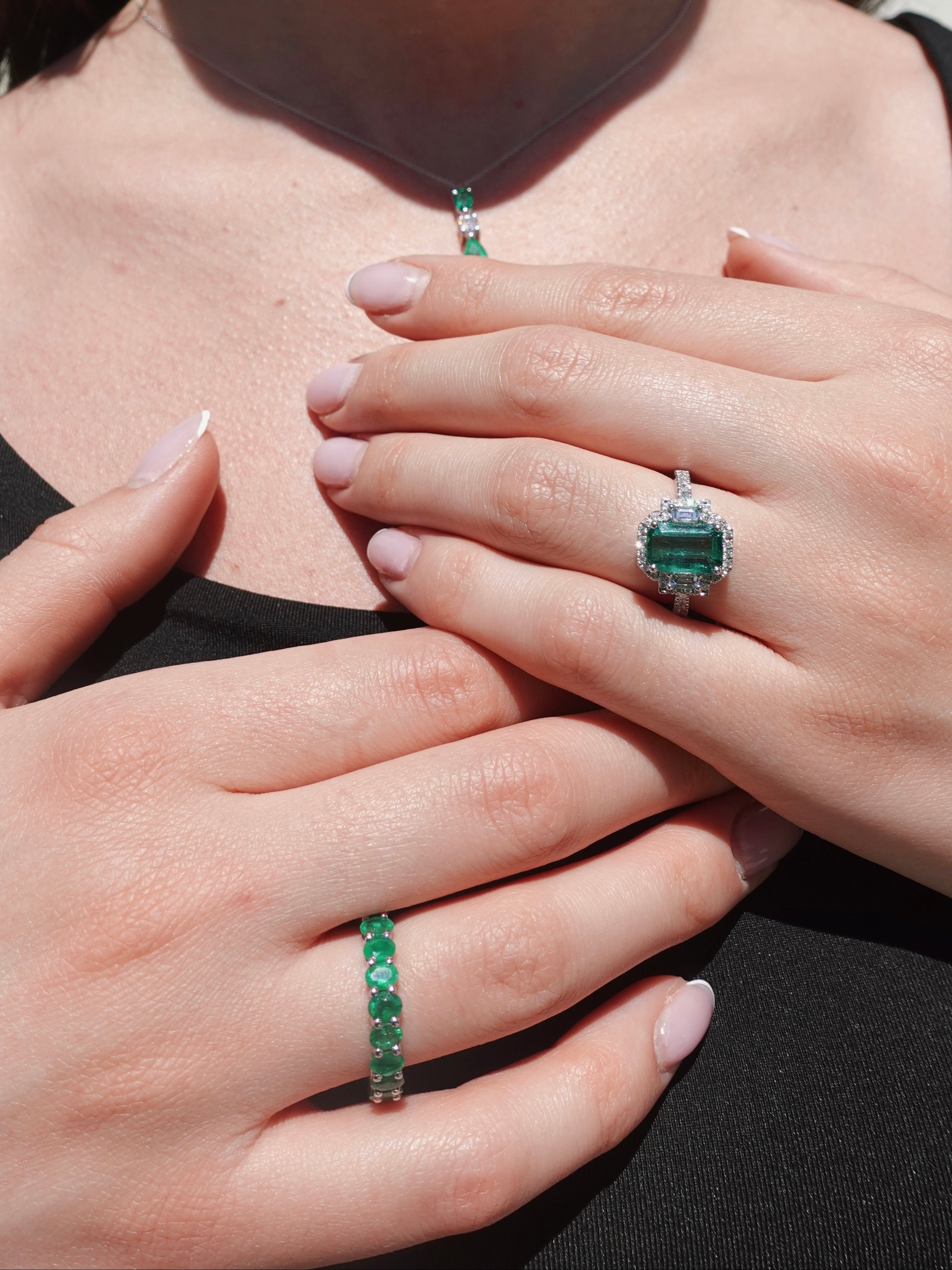 Close-up of a person wearing three emerald green gemstone rings on a plain background
