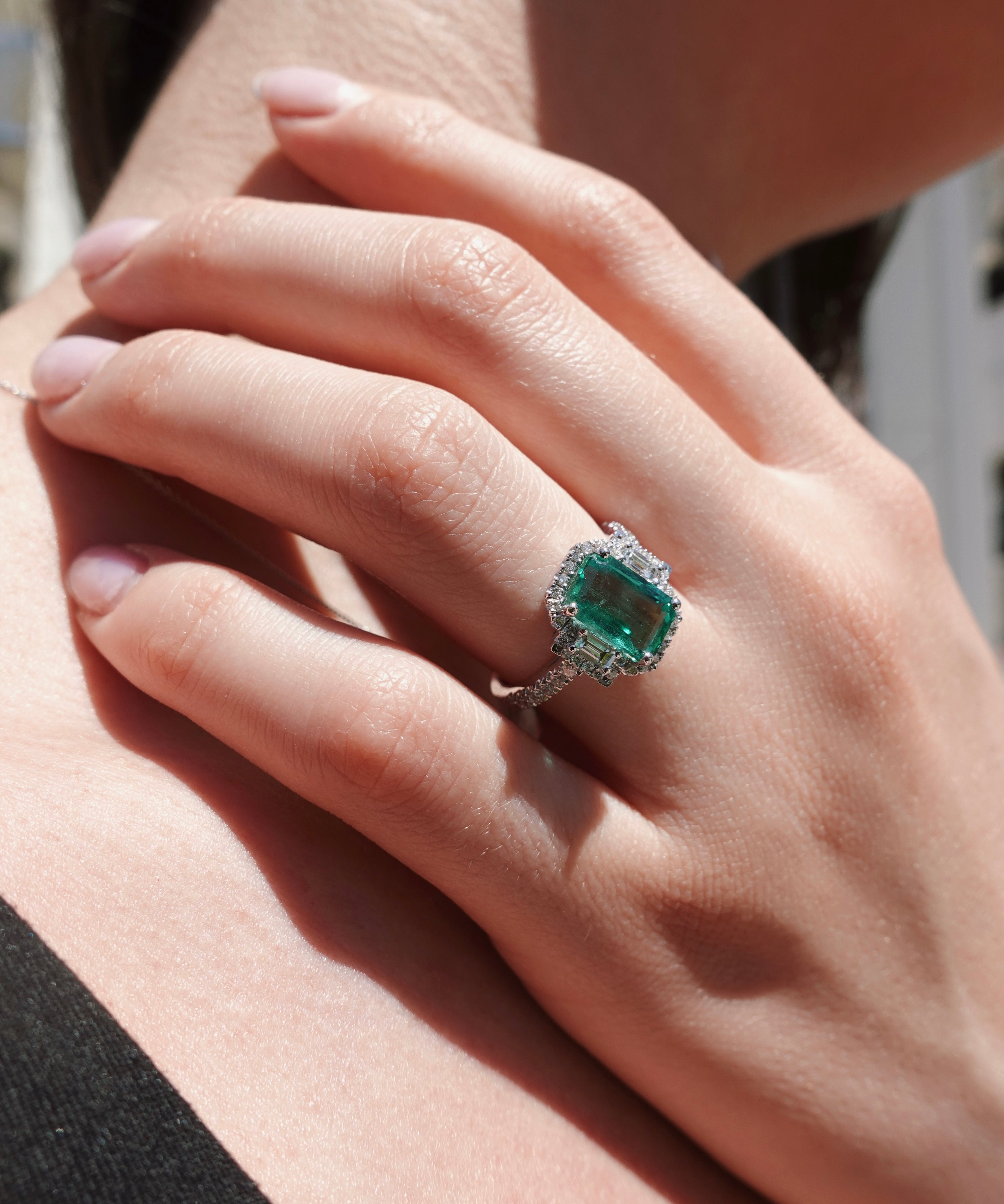 Close-up of a hand wearing an emerald ring with a blurred background