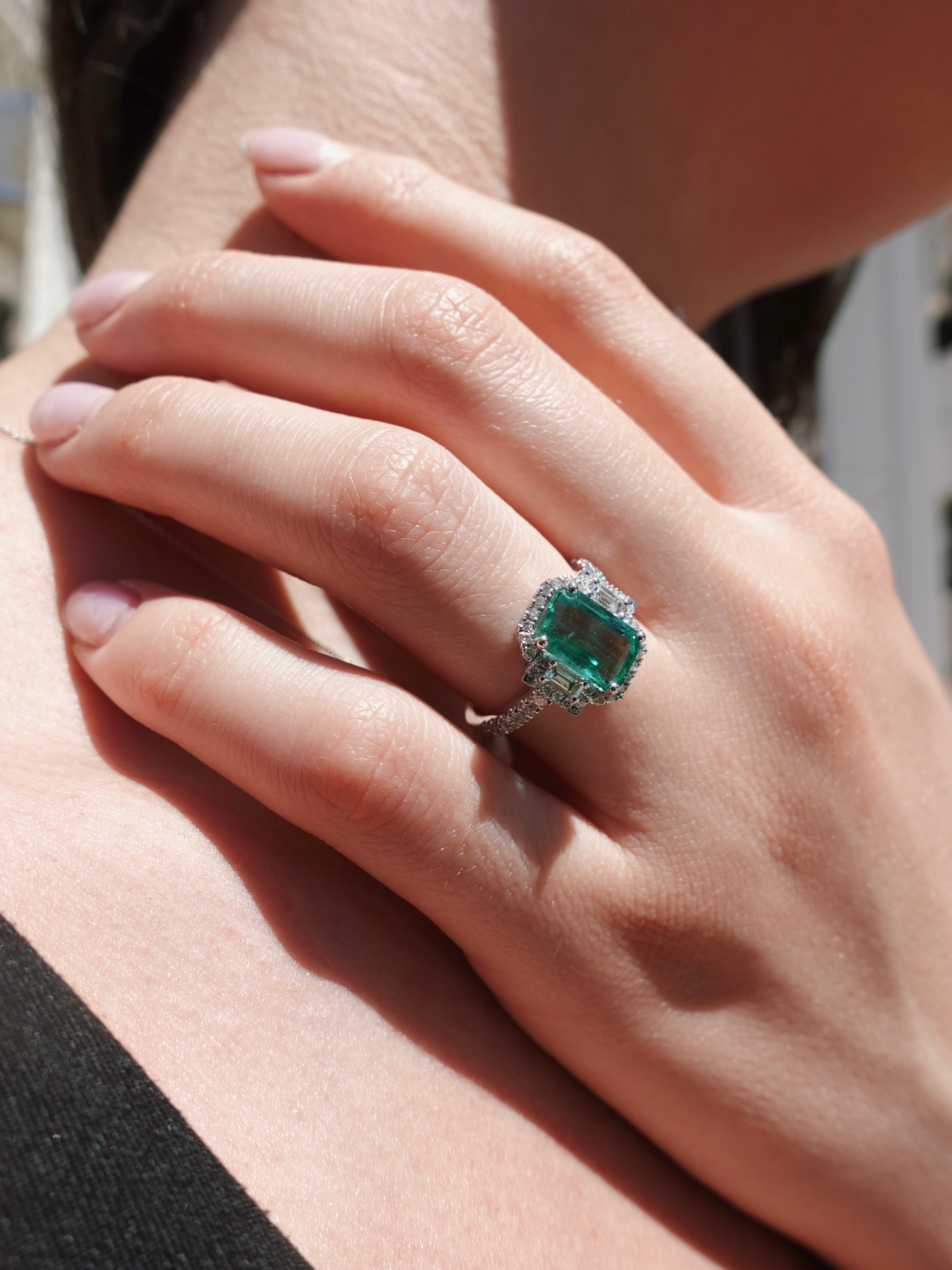 Close-up of a hand wearing an emerald ring with a blurred background