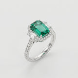 Ring with a green emerald gemstone and diamond-studded band on a light gray background