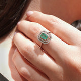 Close-up of a hand wearing an emerald ring with a diamond halo.
