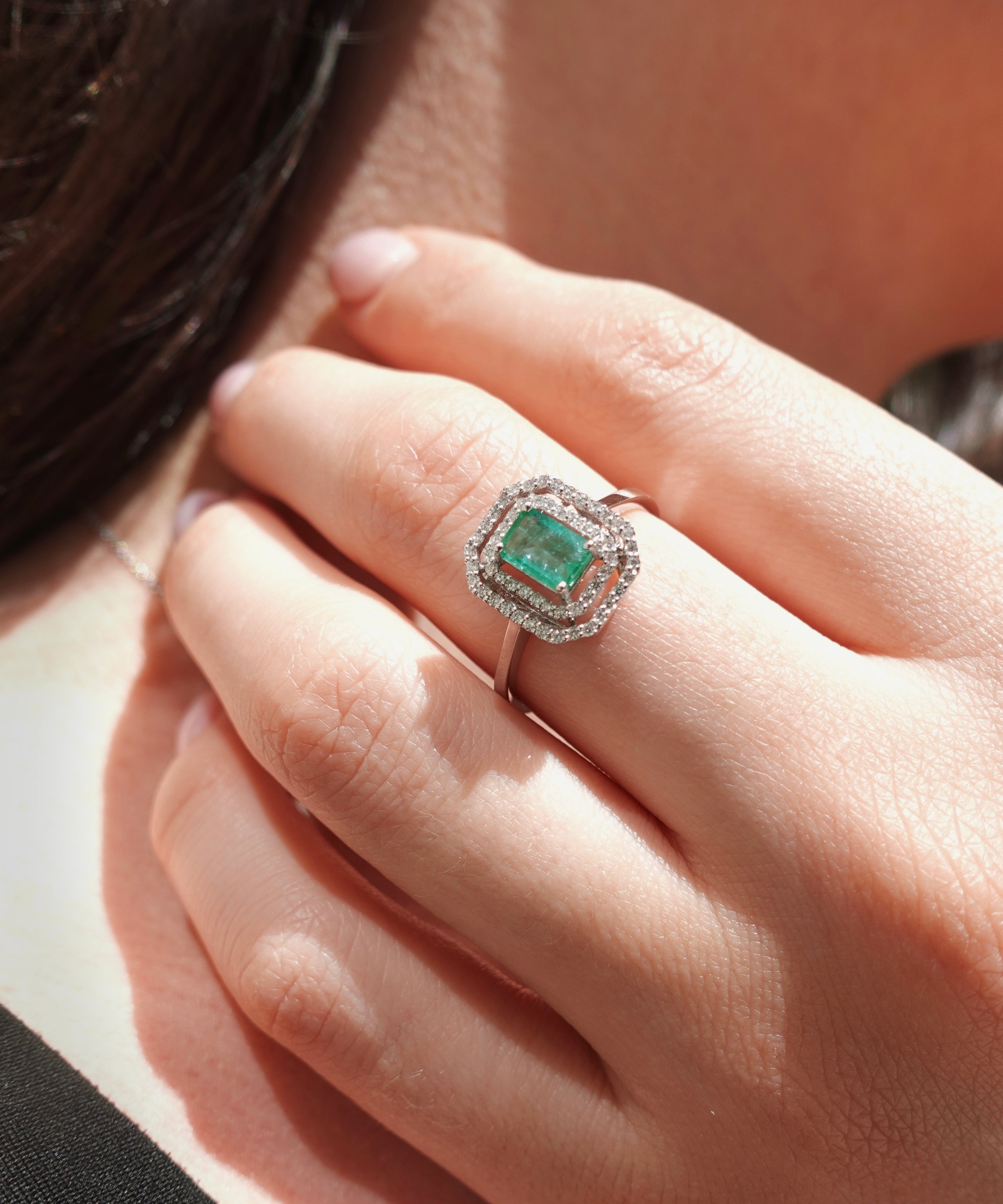 Close-up of a hand wearing an emerald ring with a diamond halo.