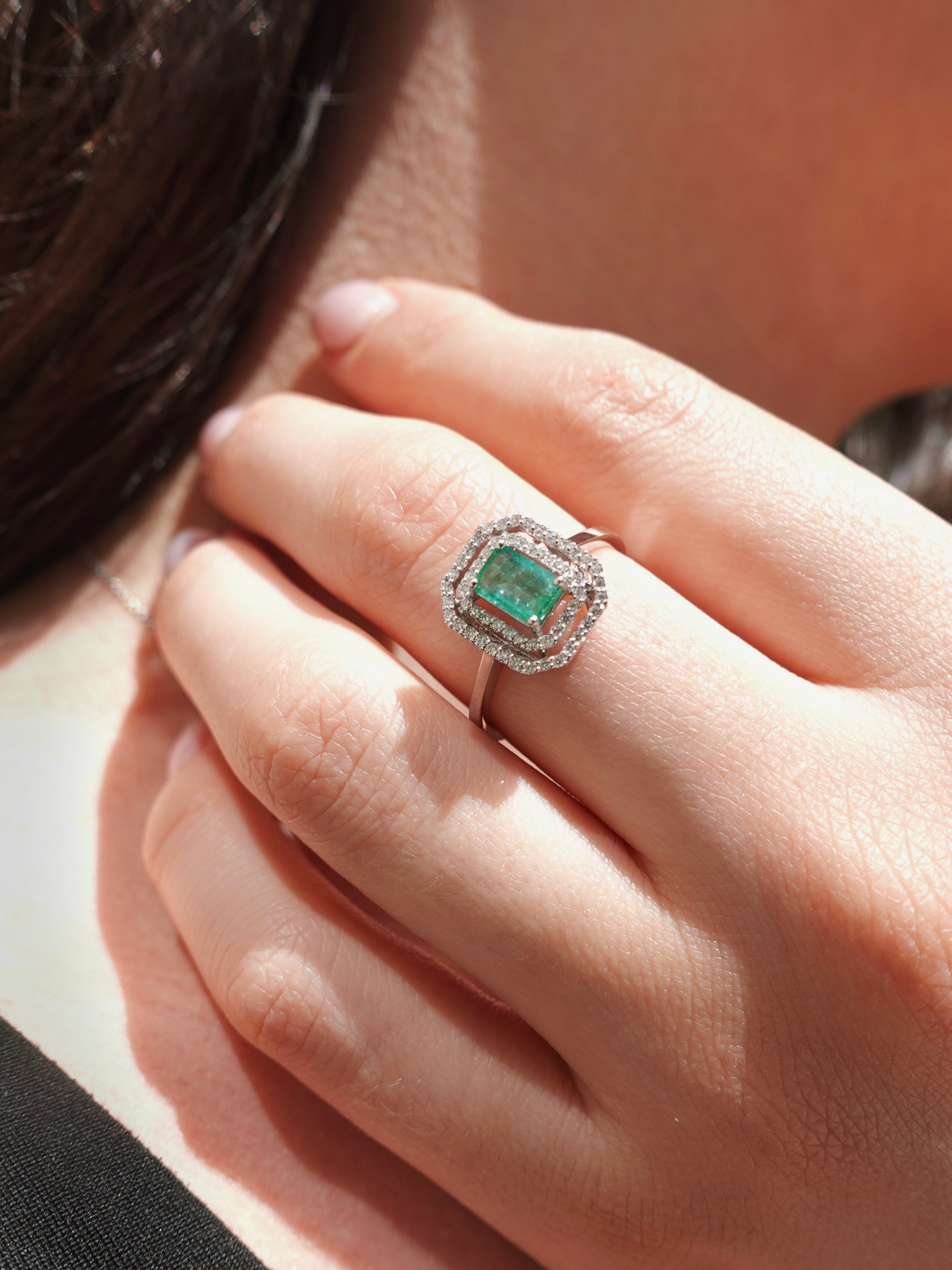 Close-up of a hand wearing an emerald ring with a diamond halo.