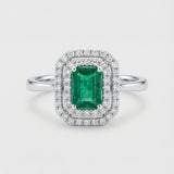 Ring with a green emerald gemstone and diamond accents on a white background