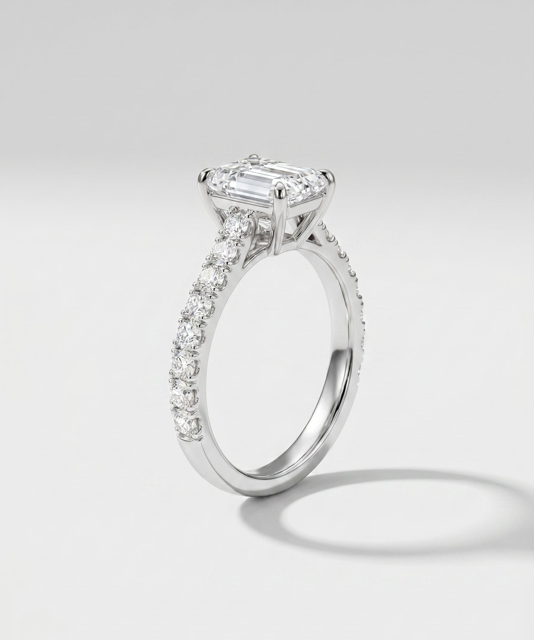 Diamond ring with a central emerald-cut diamond and smaller diamonds on a light gray background