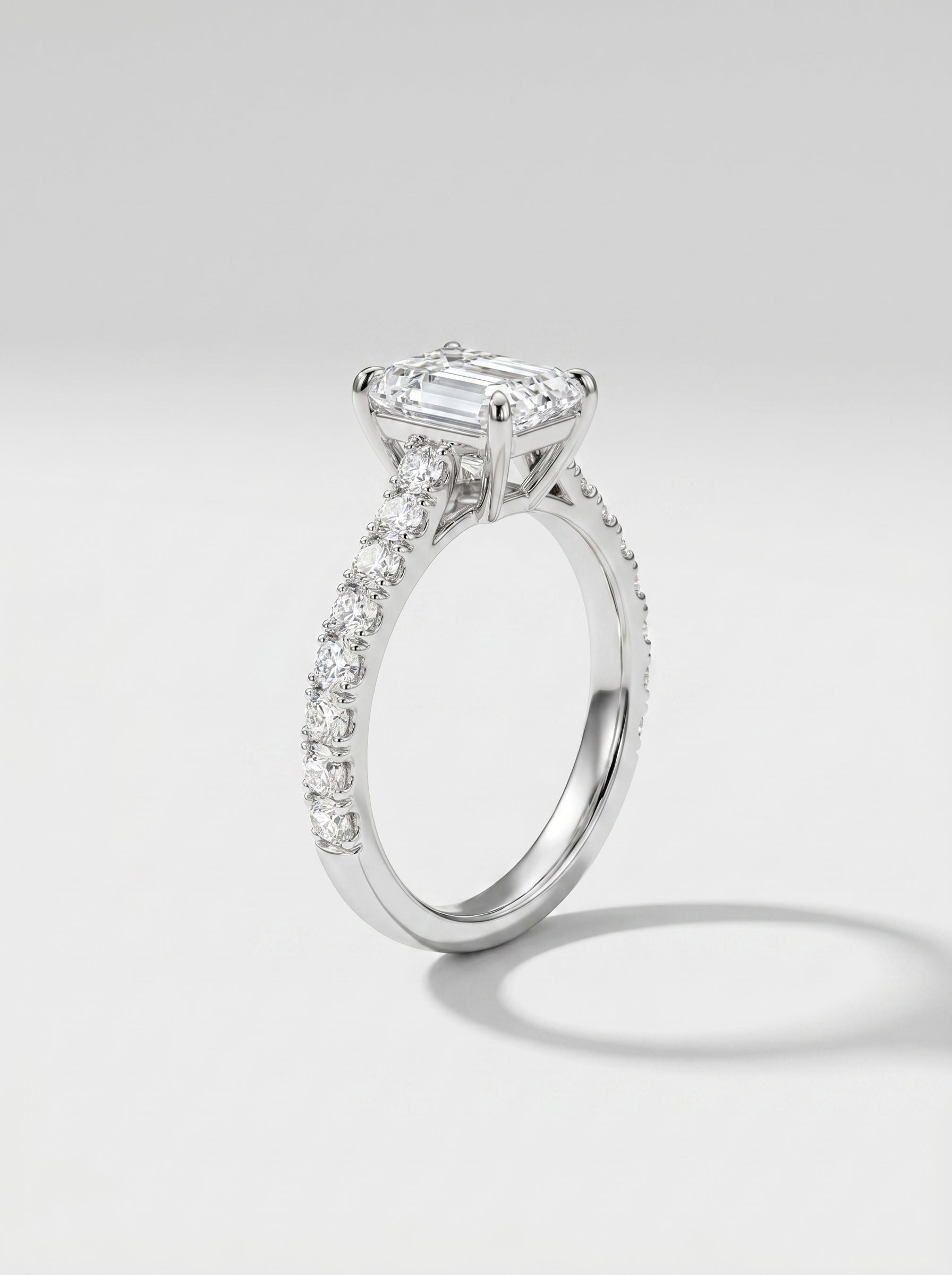 Diamond ring with a central emerald-cut diamond and smaller diamonds on a light gray background