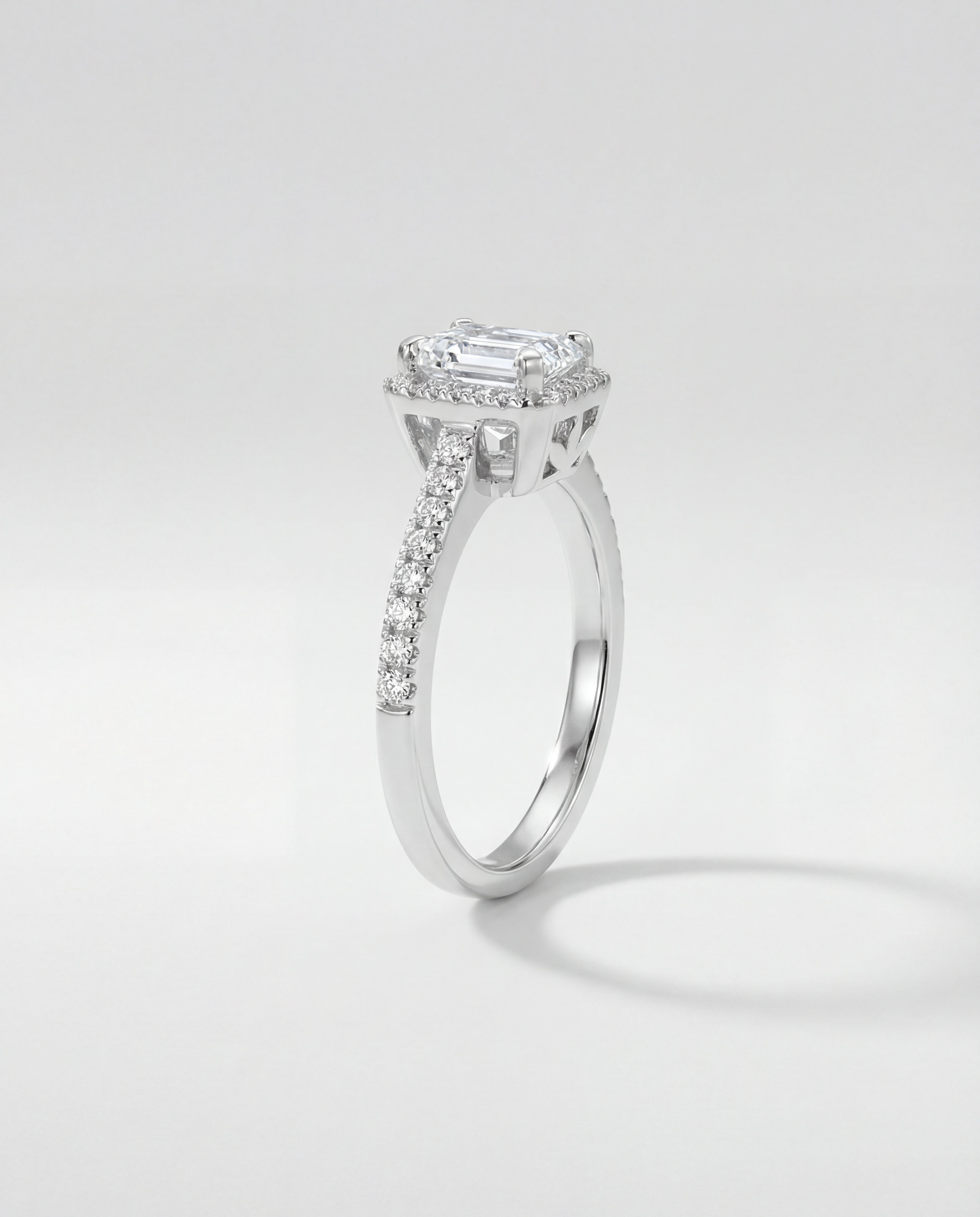 Emerald-cut halo engagement ring with a diamond on a light gray background