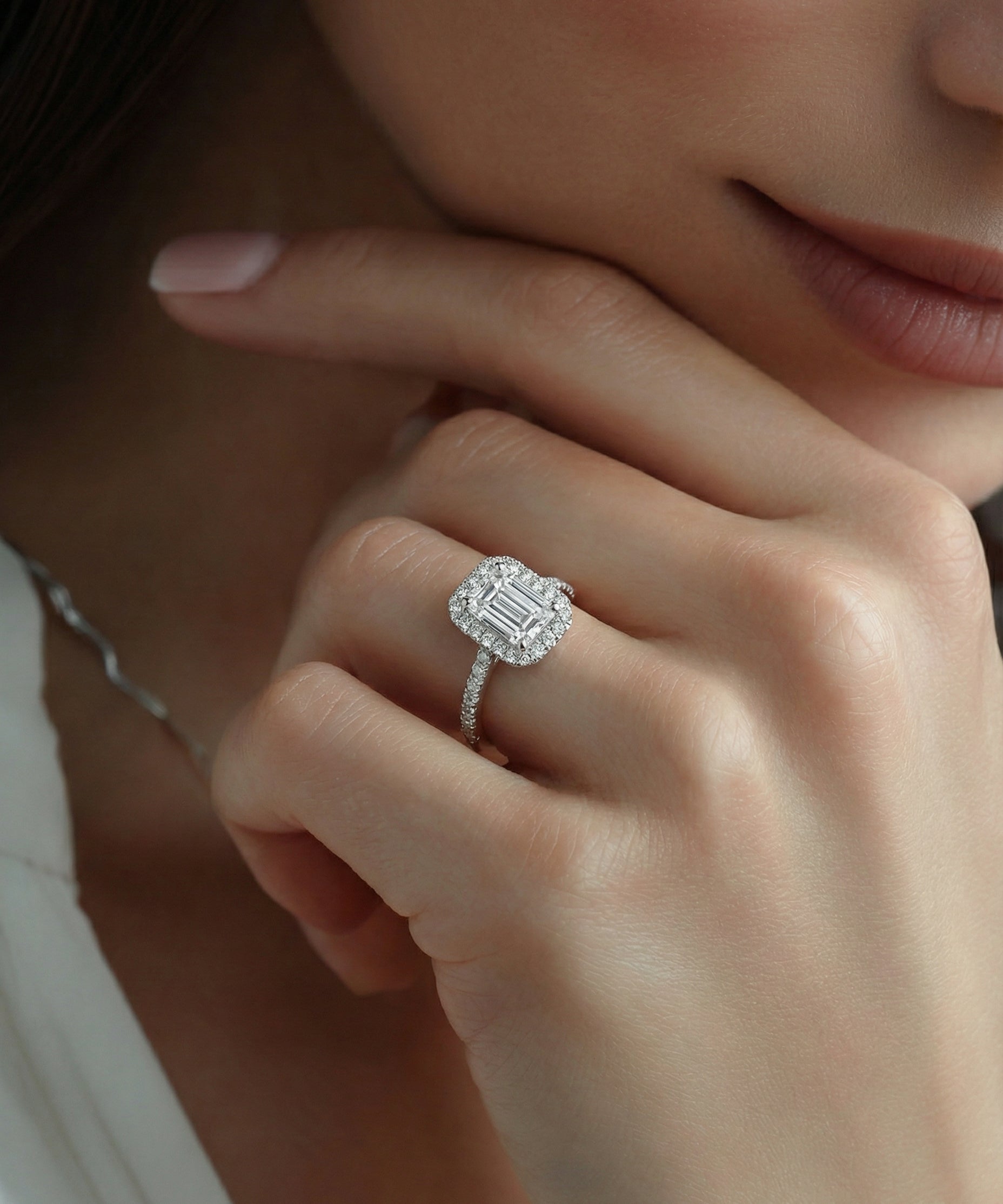Close-up of a hand wearing an emerald-cut diamond ring with a soft focus background