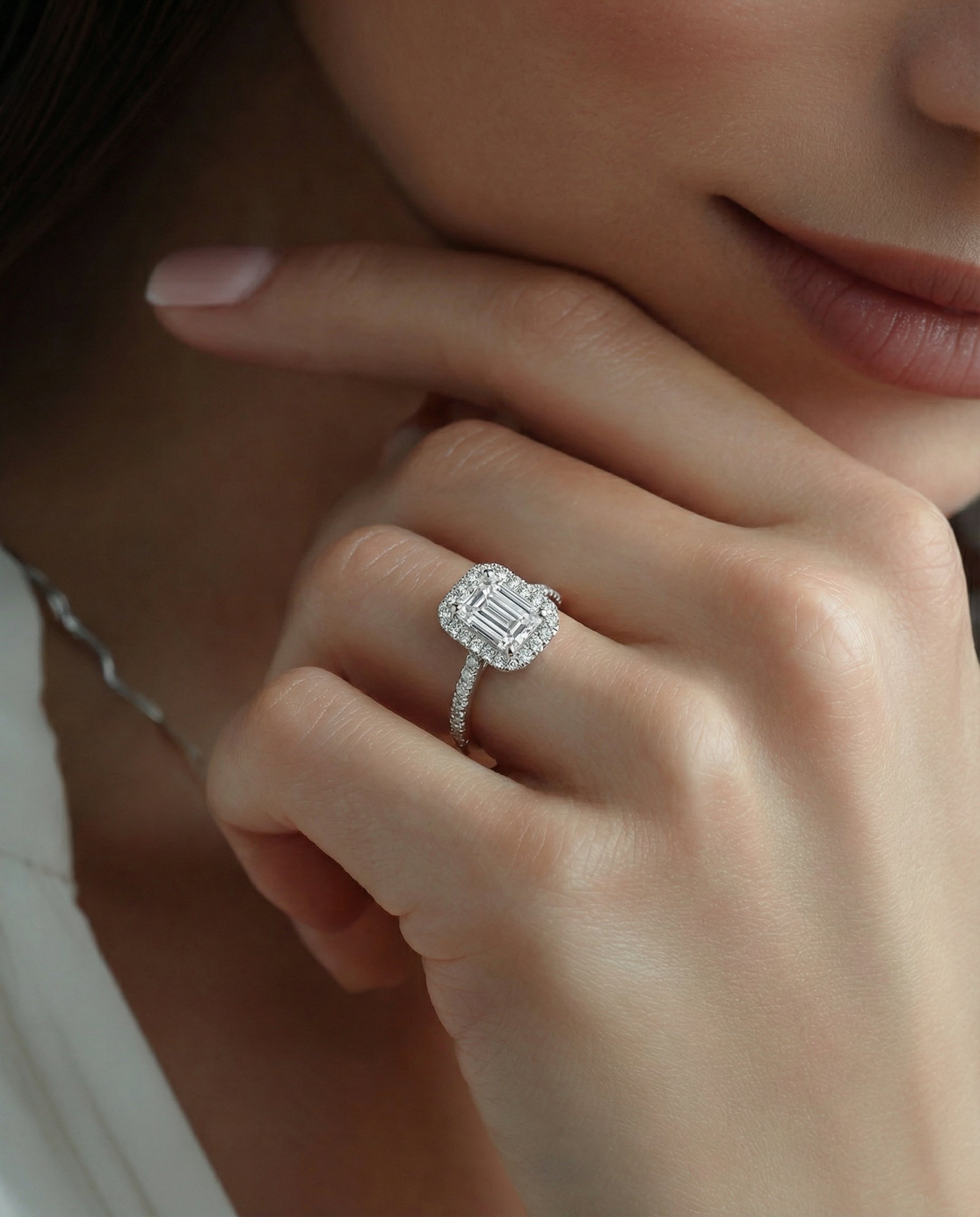 Close-up of a hand wearing an emerald-cut diamond ring with a soft focus background
