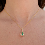 Gold necklace with a green emerald gemstone pendant on a person's neck