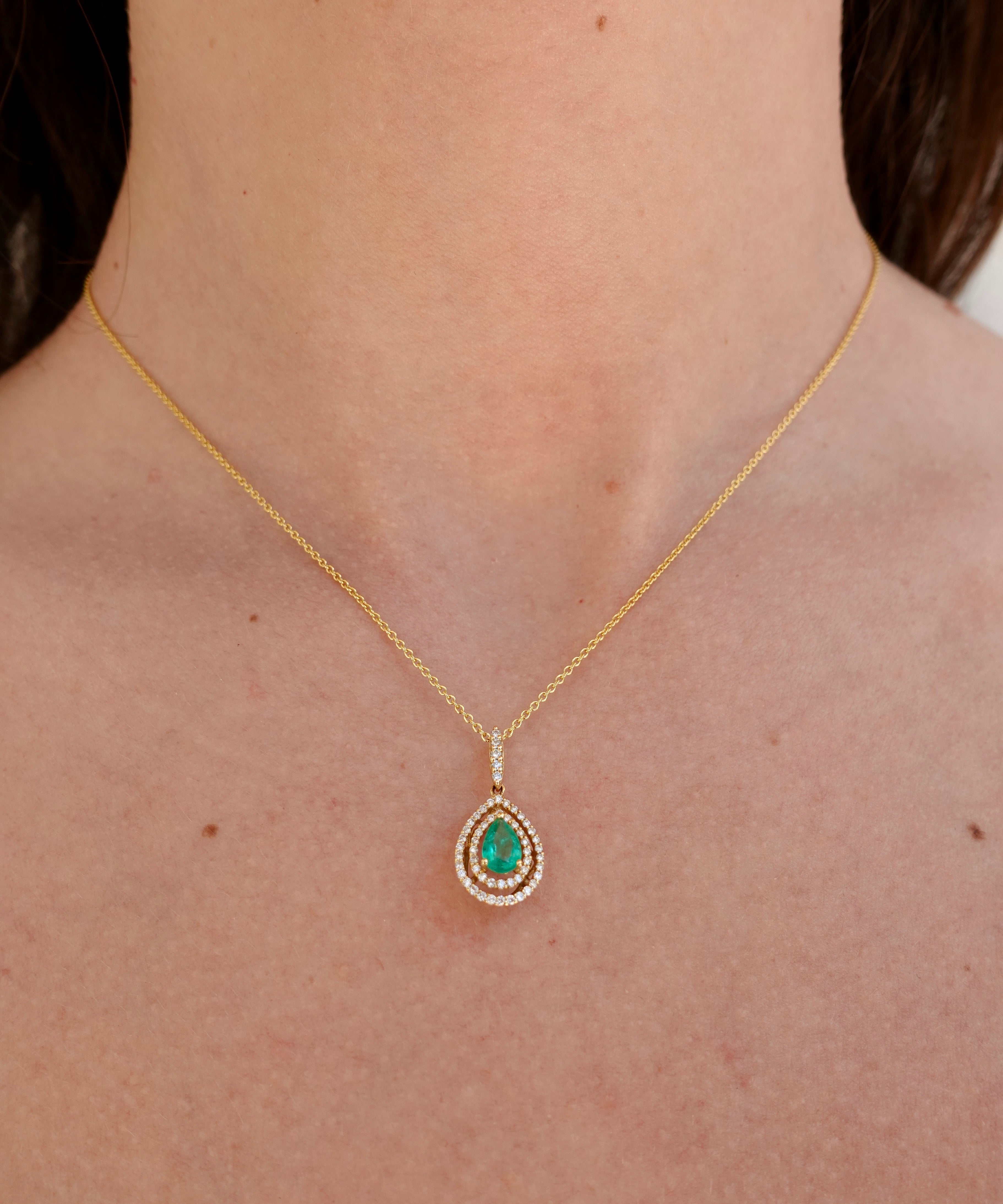 Gold necklace with a green emerald gemstone pendant on a person's neck