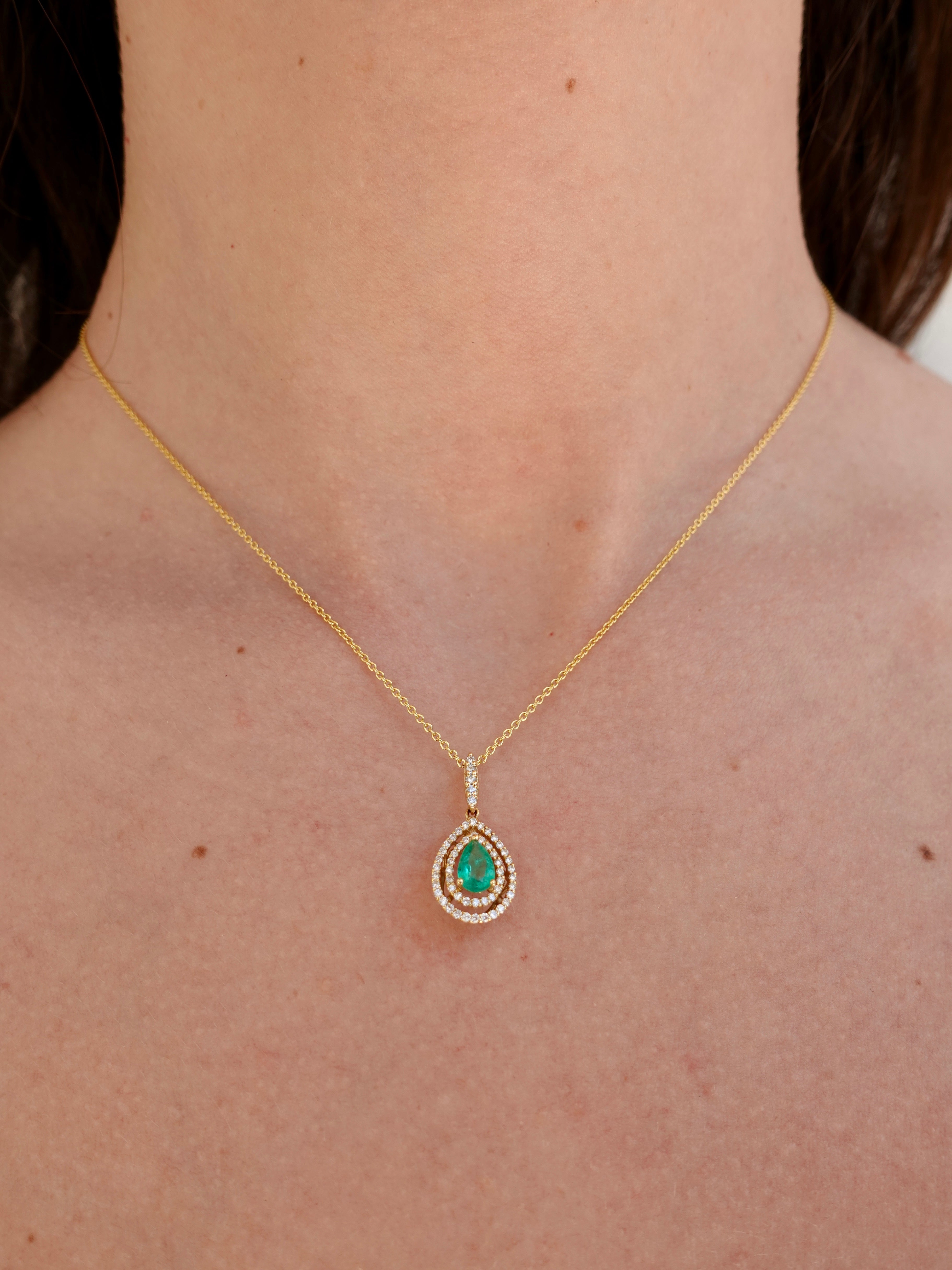 Gold necklace with a green emerald gemstone pendant on a person's neck