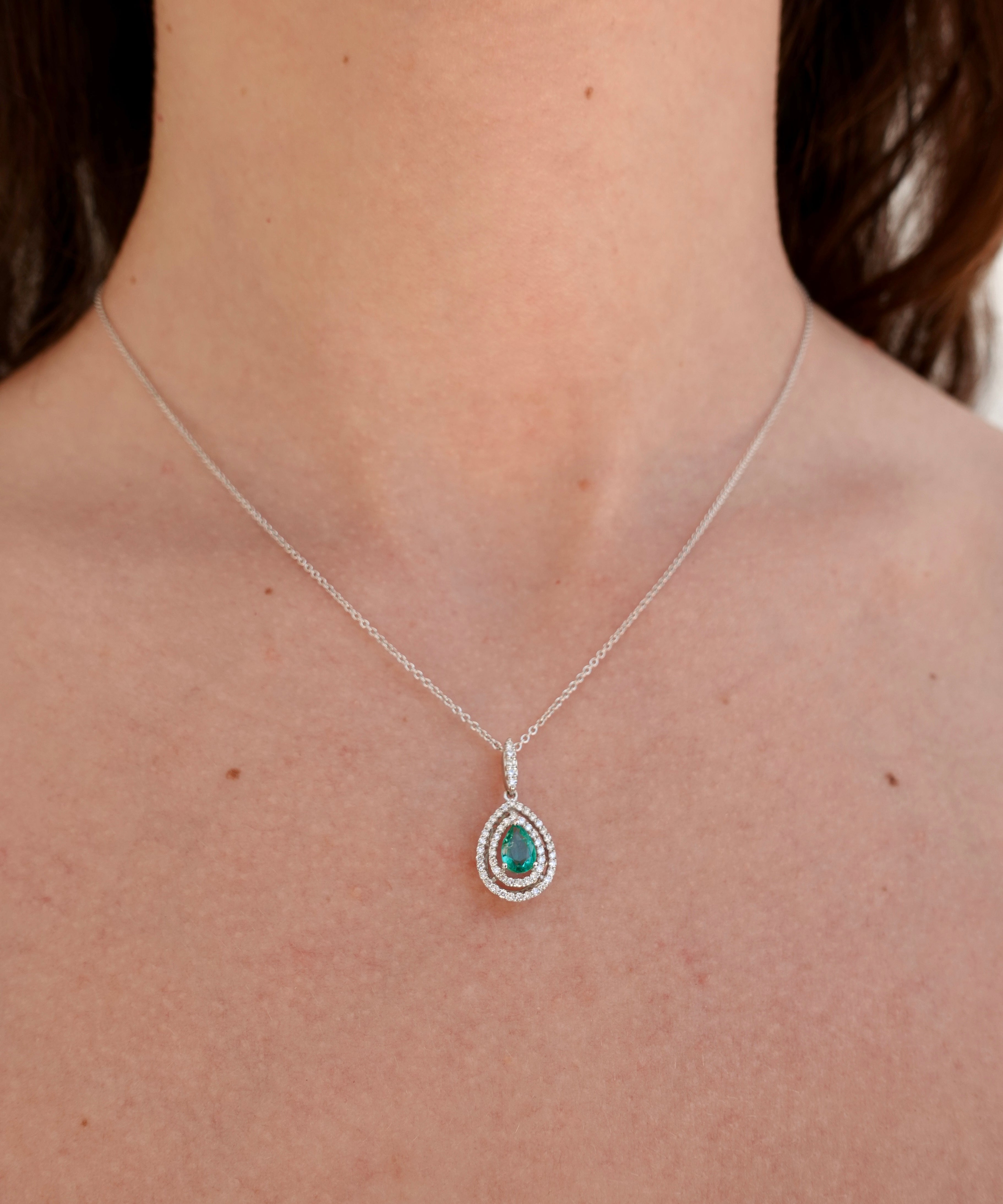 Necklace with a pendant featuring a green emerald gemstone on a person's neck.