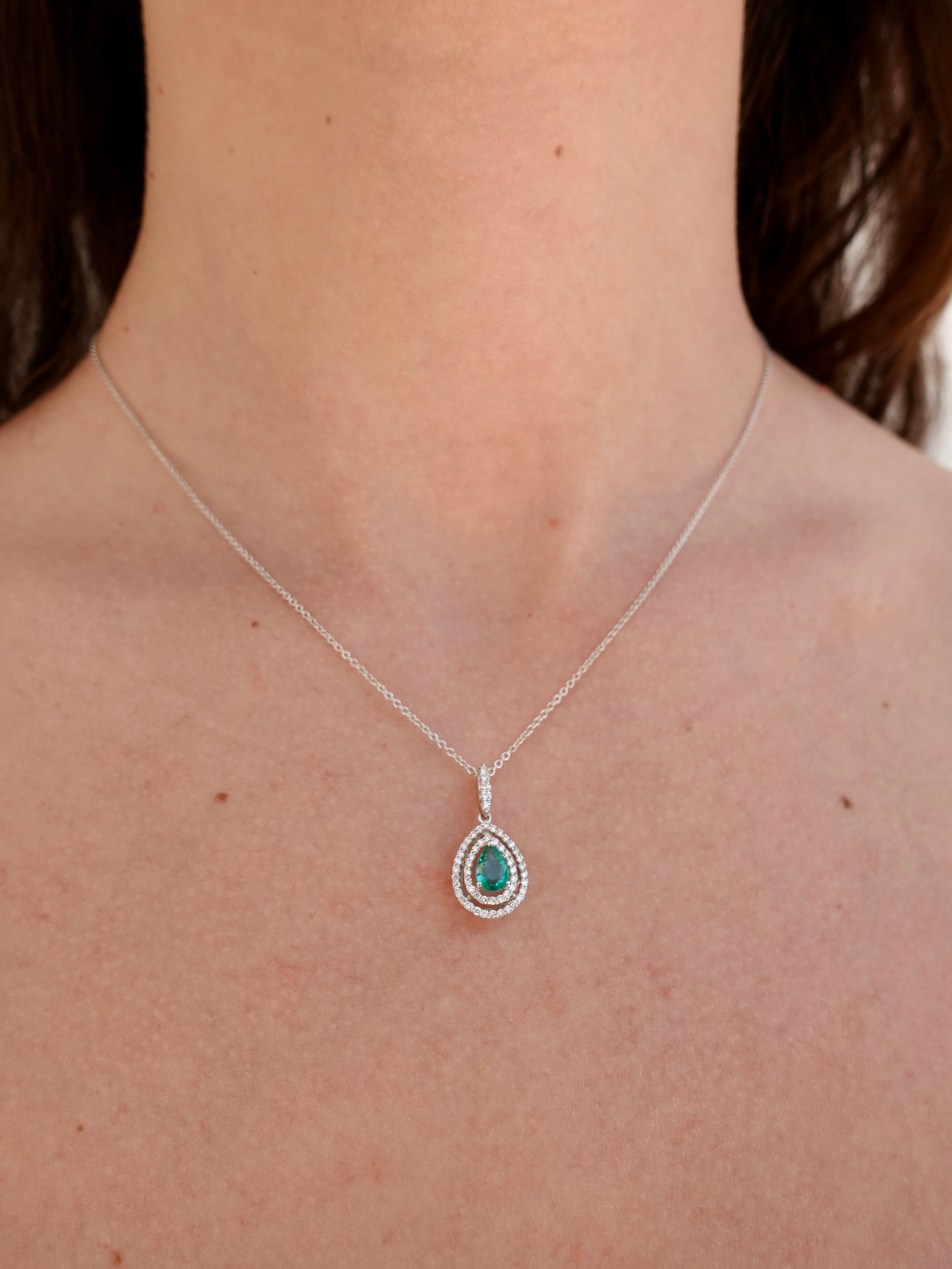 Necklace with a pendant featuring a green emerald gemstone on a person's neck.