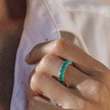 Close-up of a hand wearing an eternity emerald ring with a blurred background
