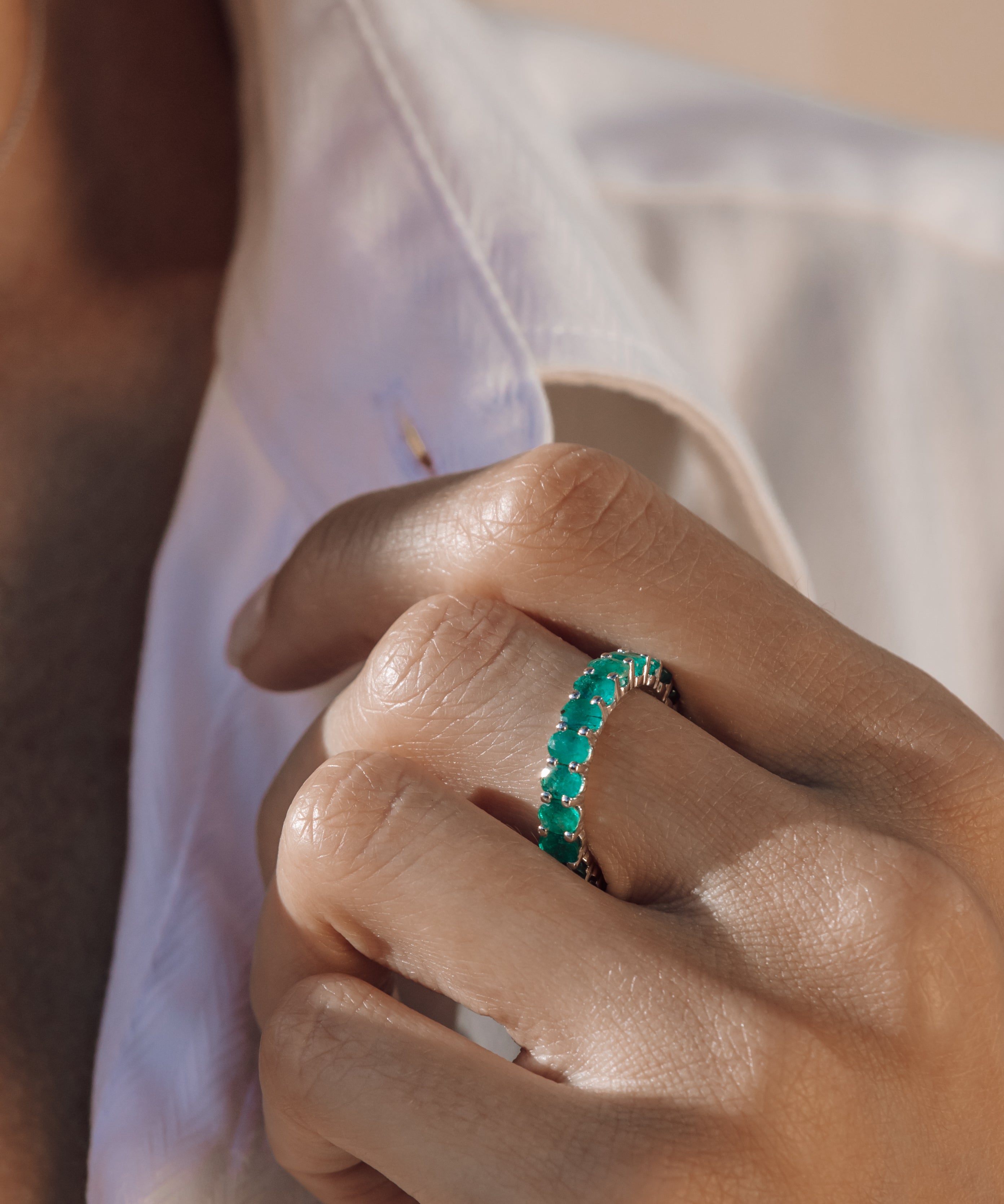 Close-up of a hand wearing an eternity emerald ring with a blurred background