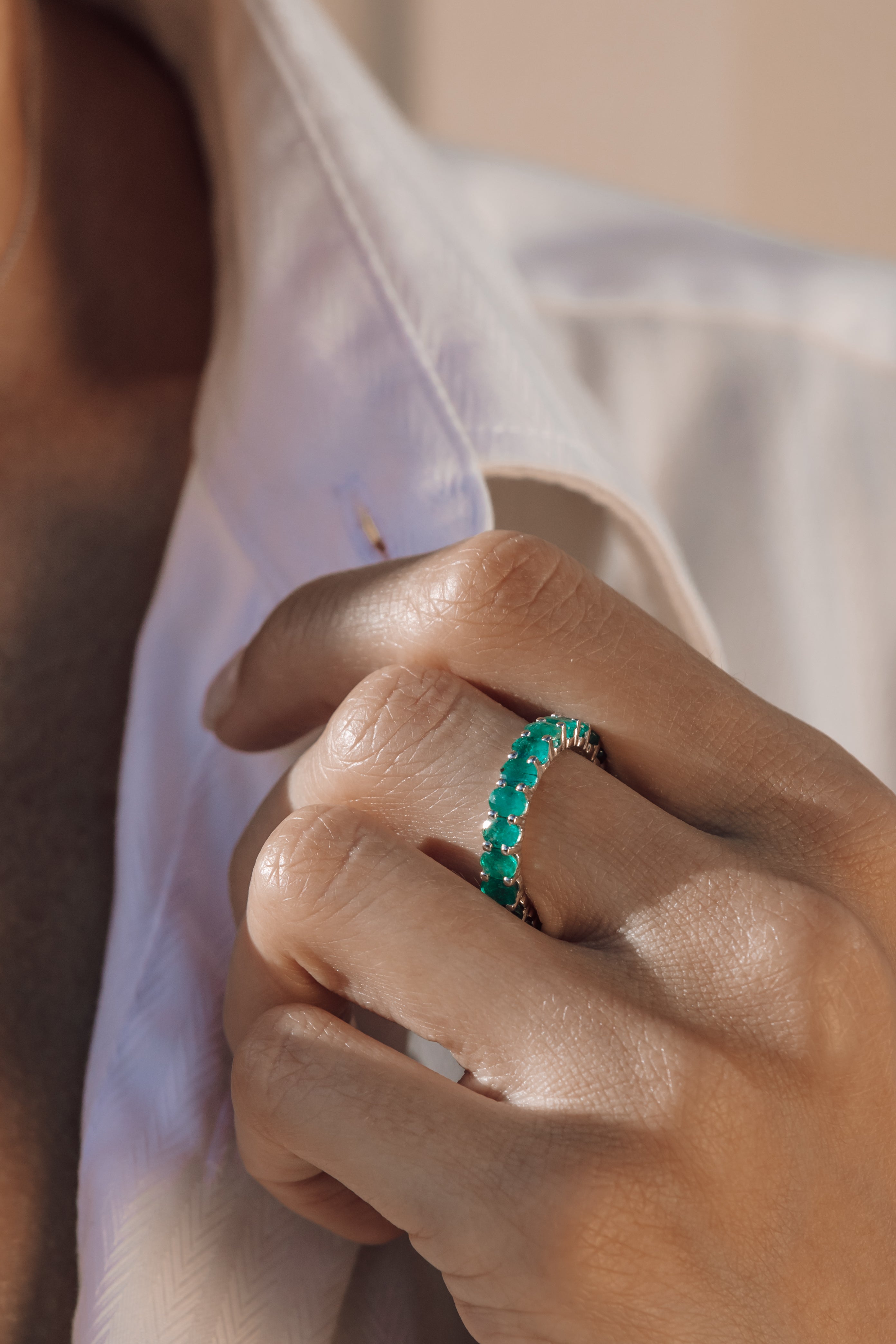 Close-up of a hand wearing an eternity emerald ring with a blurred background