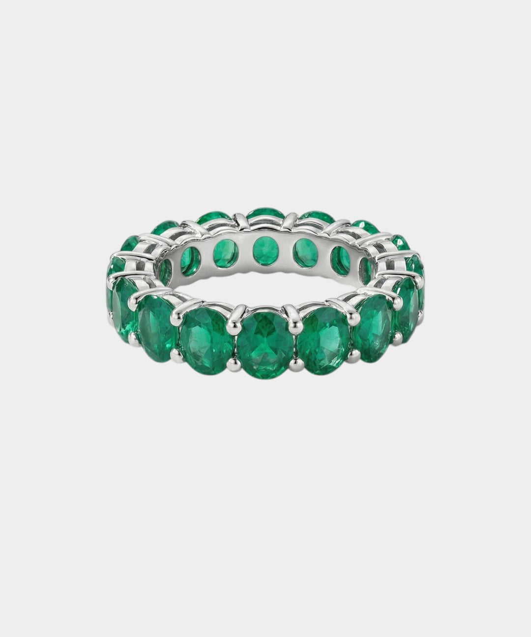 white gold ring with green emerald gemstones on a light gray background