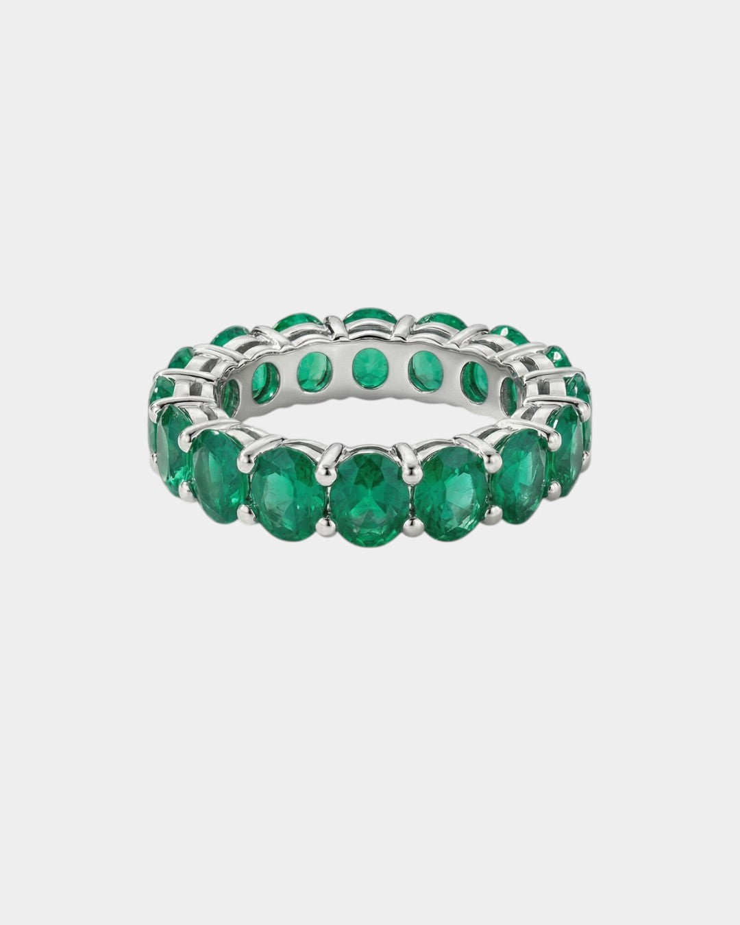 white gold ring with green emerald gemstones on a light gray background
