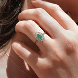 Close-up of a hand wearing an emerald and diamond ring.