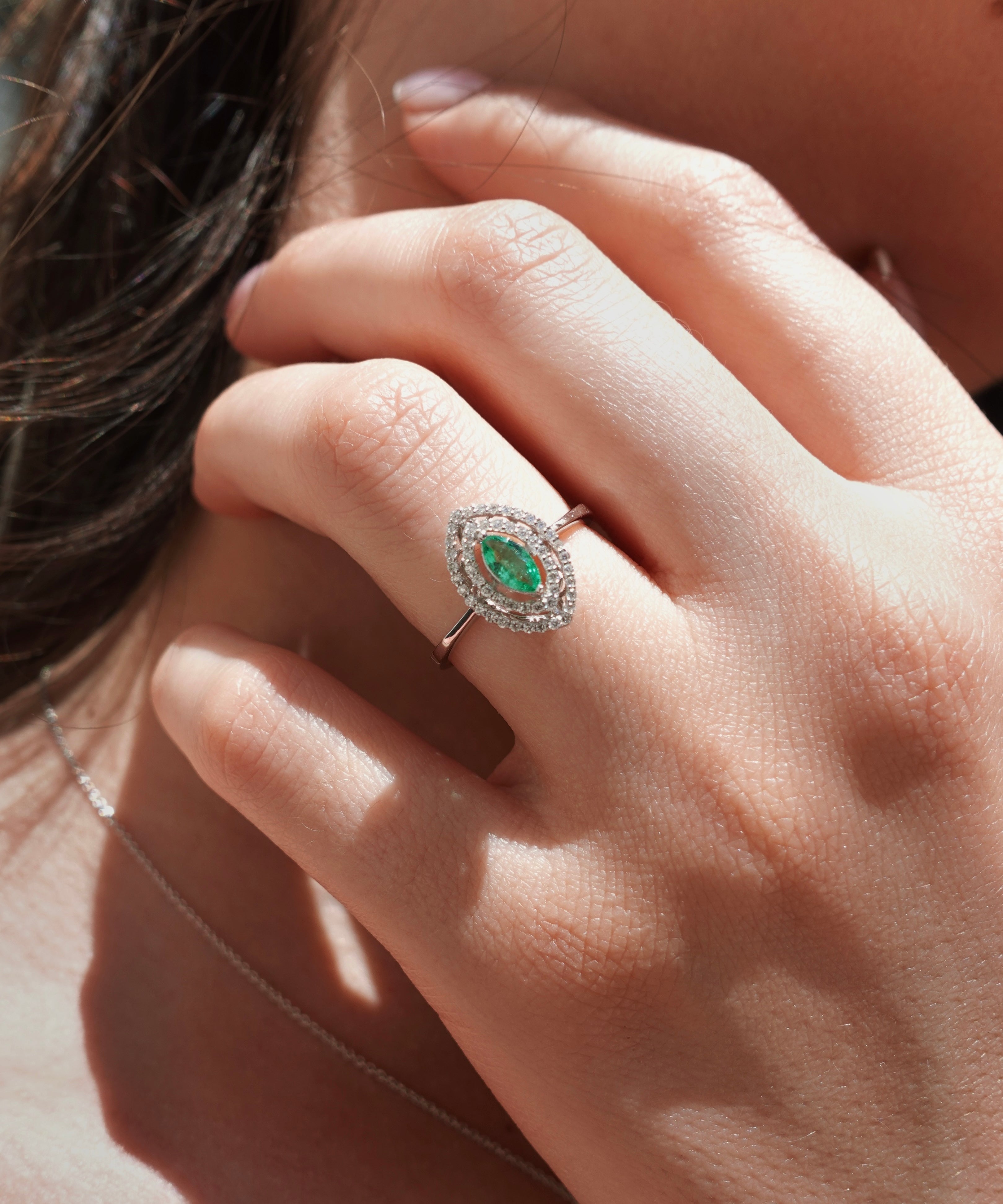 Close-up of a hand wearing an emerald and diamond ring.