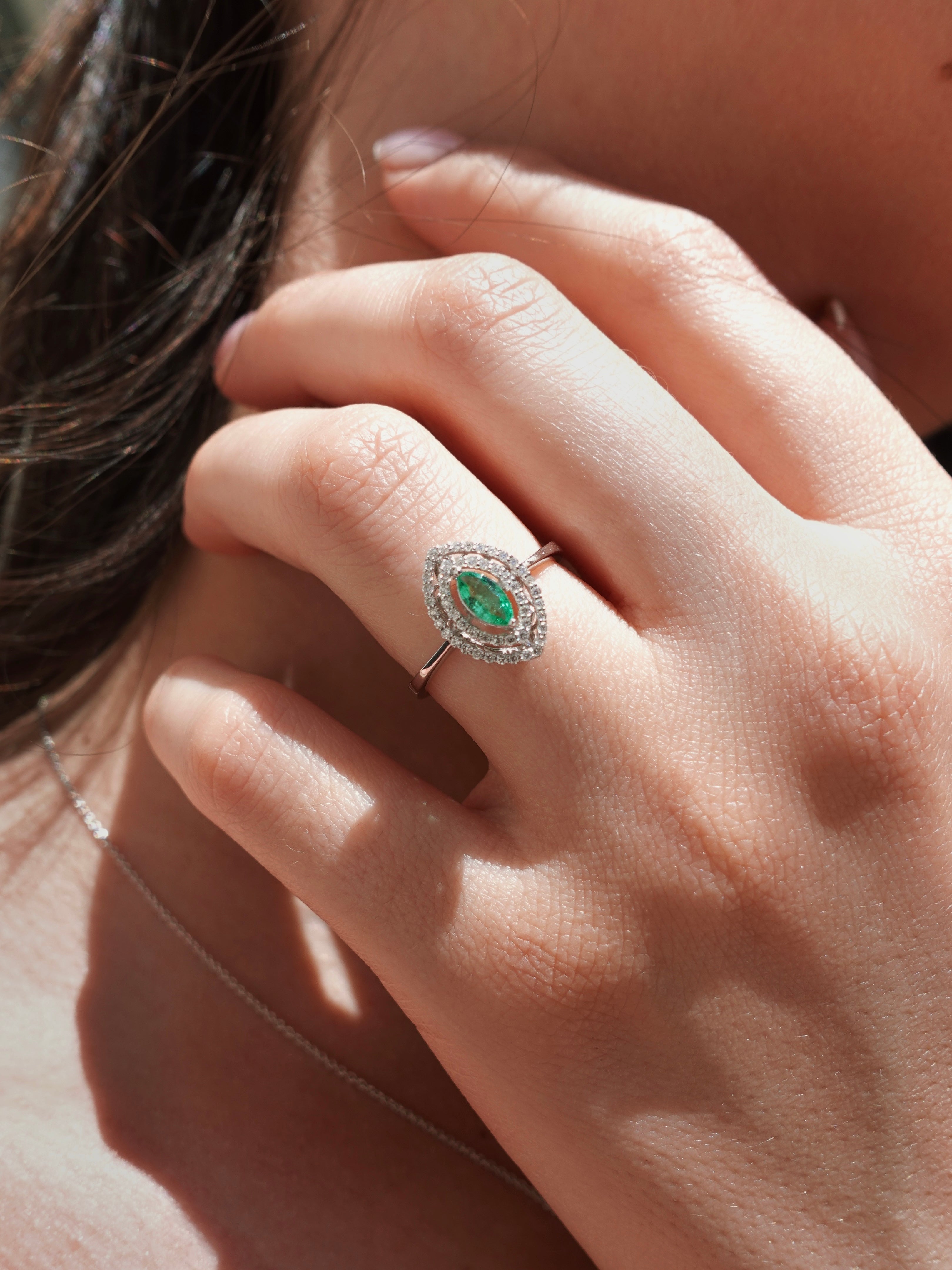 Close-up of a hand wearing an emerald and diamond ring.
