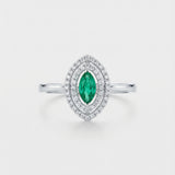 Ring with a green emerald gemstone and diamond accents on a light gray background